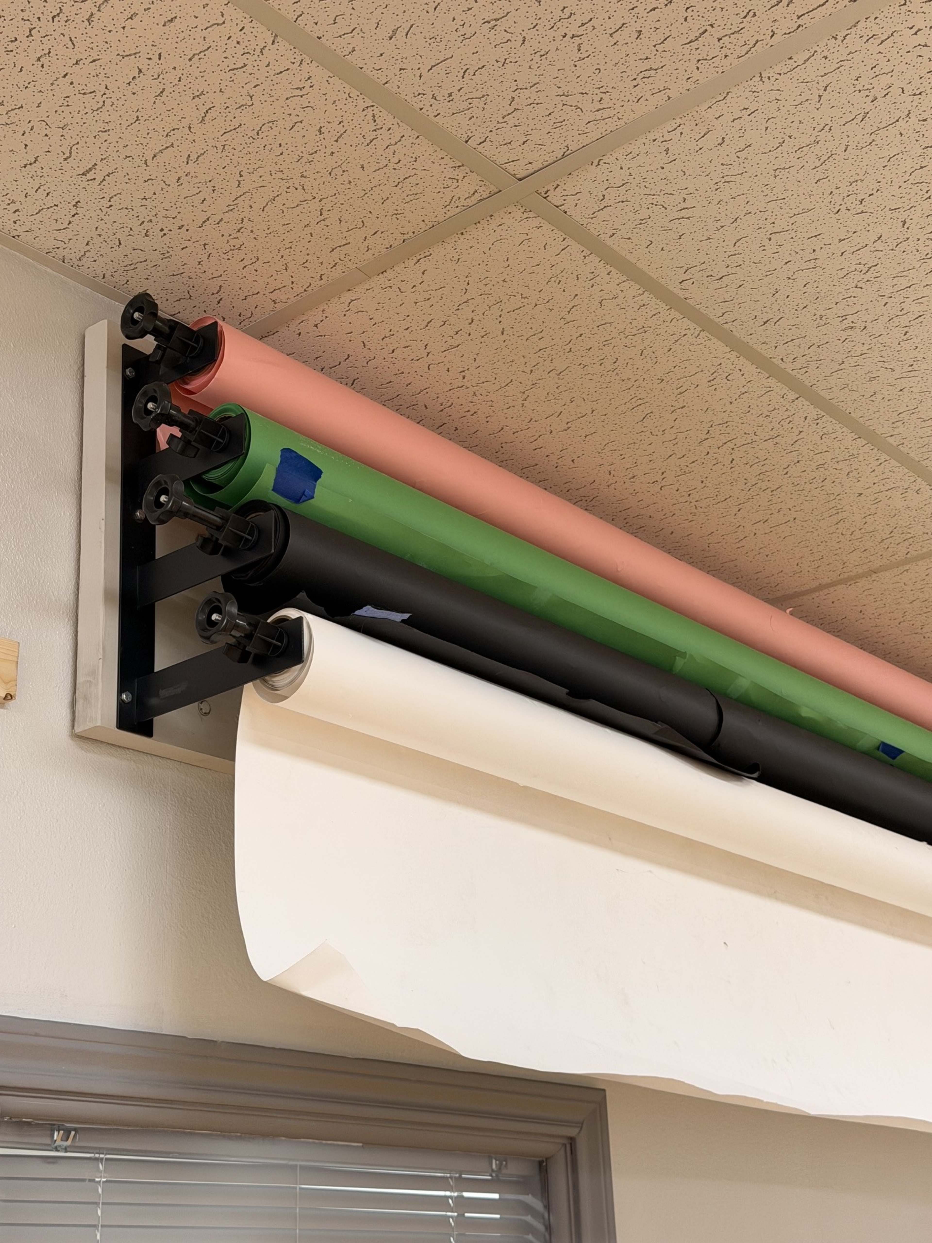 The image shows rolls of colored paper, including pink, green, black, and white, mounted on a wall rack.