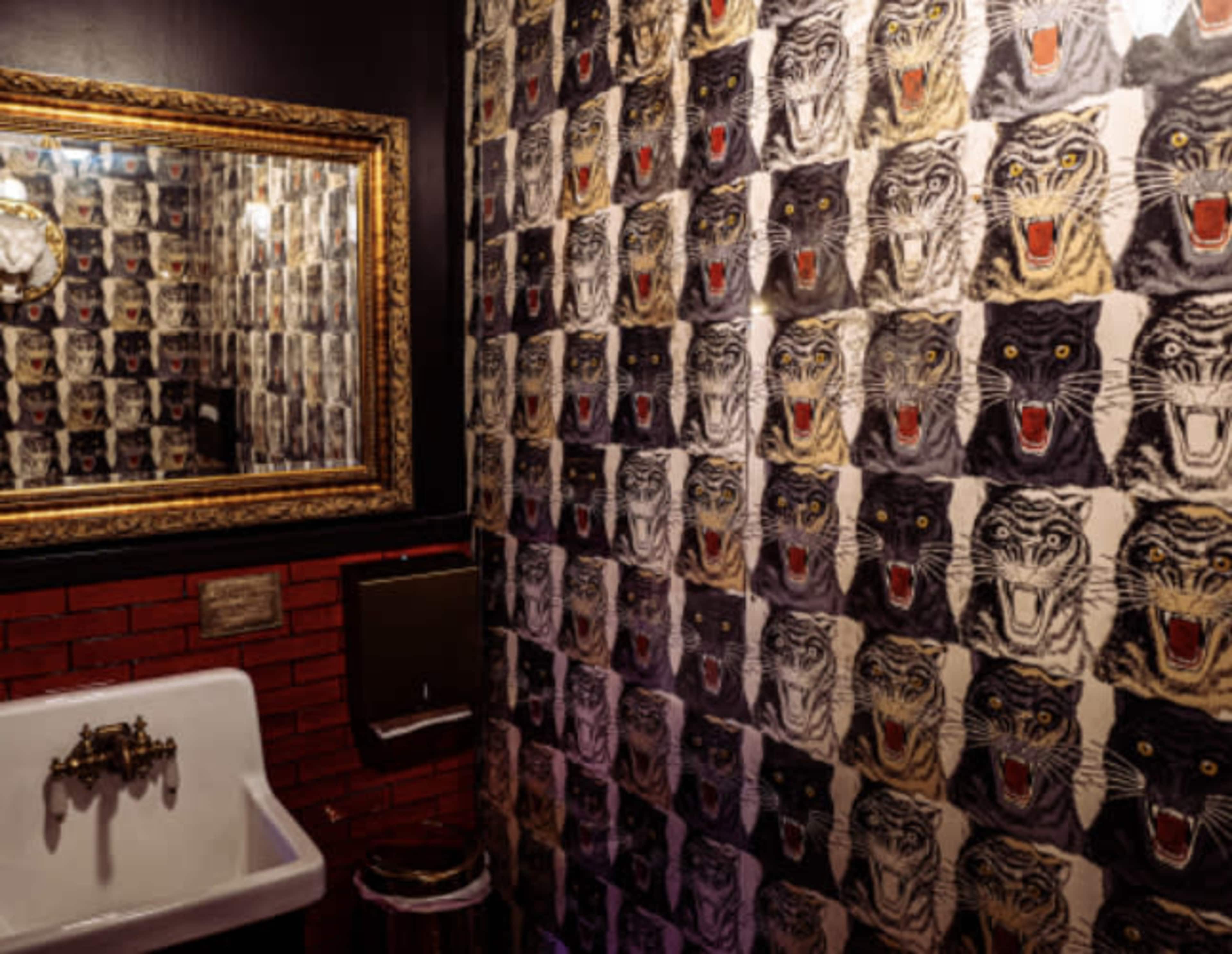 A bathroom with a vintage sink and a wall covered in a patterned wallpaper featuring large tiger faces, accompanied by a decorative mirror.