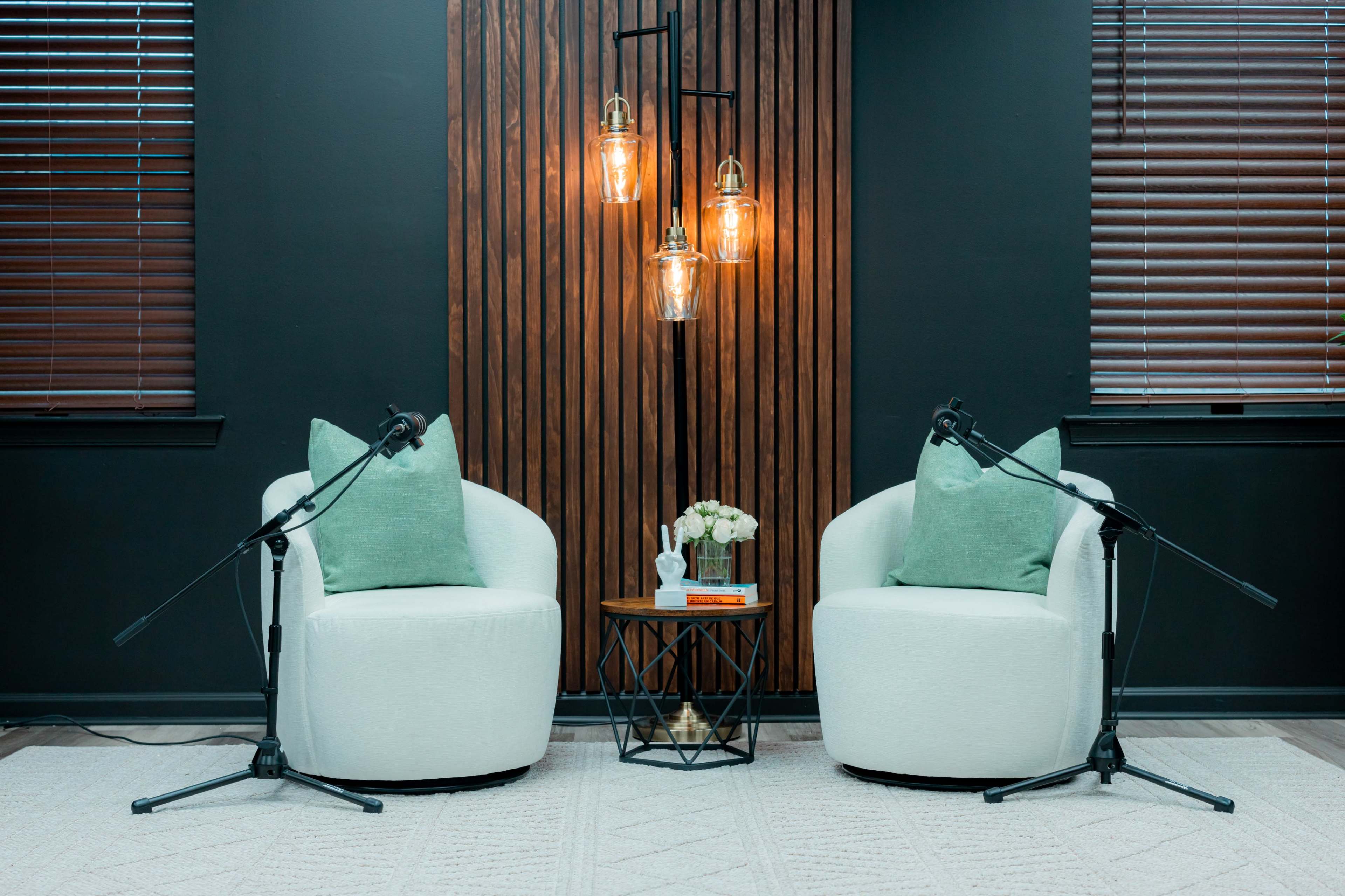 The image depicts two white chairs with green cushions positioned facing each other under a multi-light fixture, with a small table and floral arrangement between them.