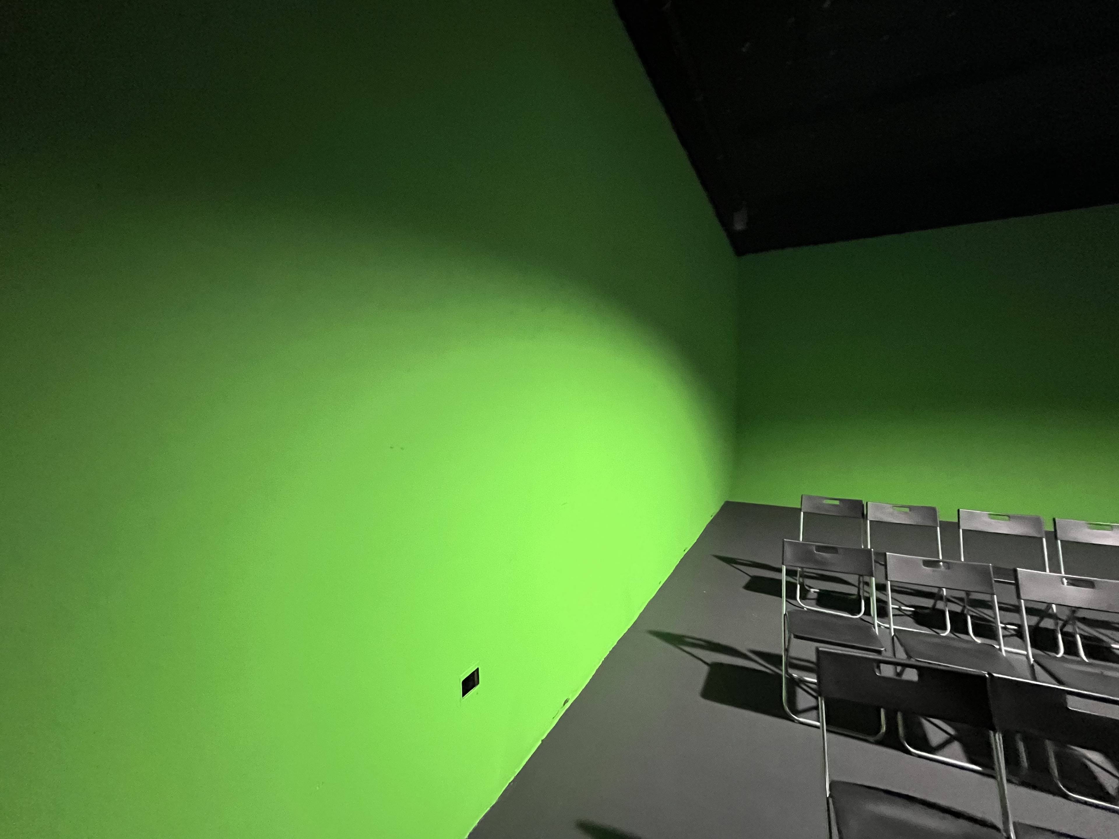 A room with bright green walls and a row of metal chairs arranged against one wall.