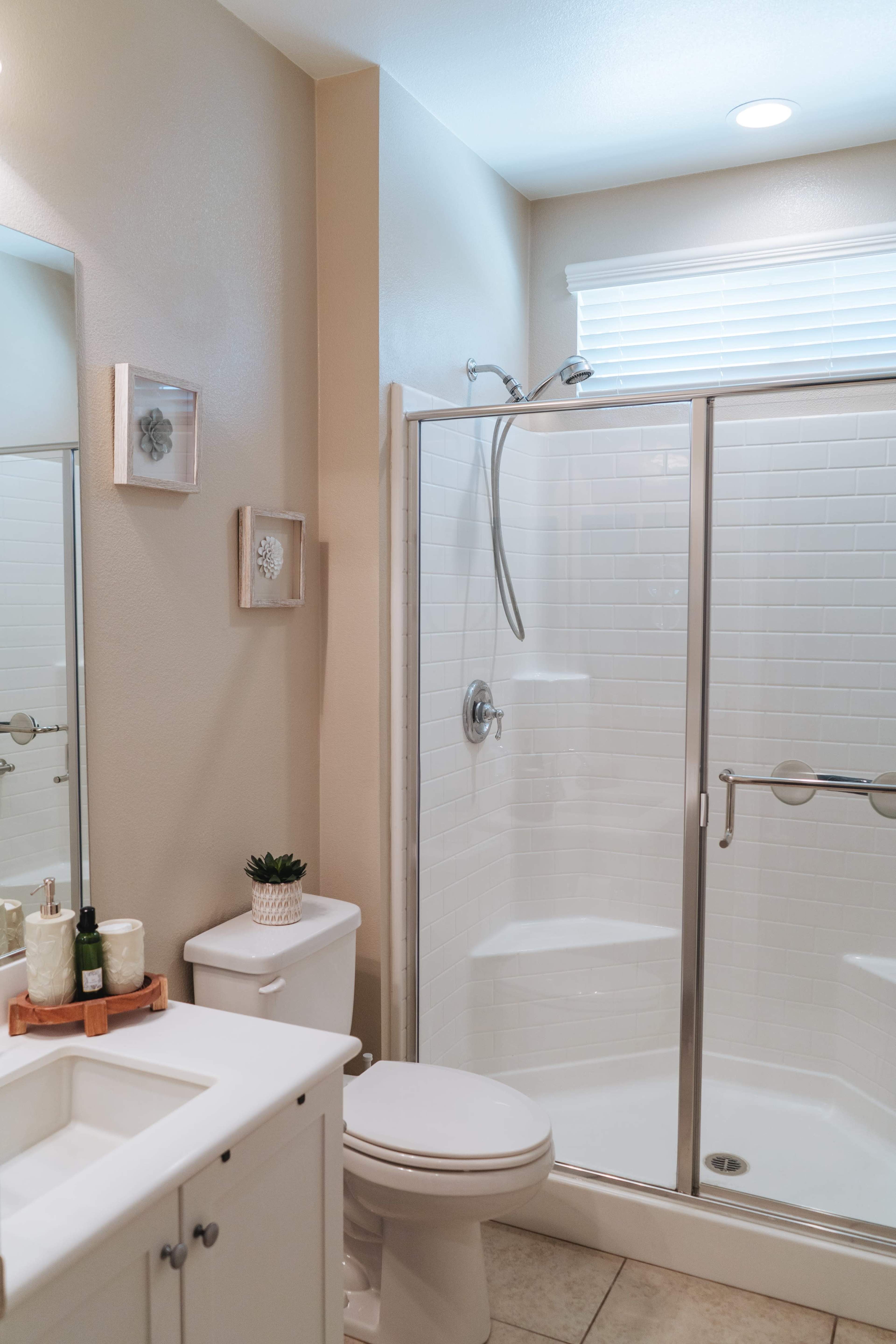 A modern bathroom features a shower stall with glass doors, a white toilet, and a sink with a wooden tray holding toiletries.