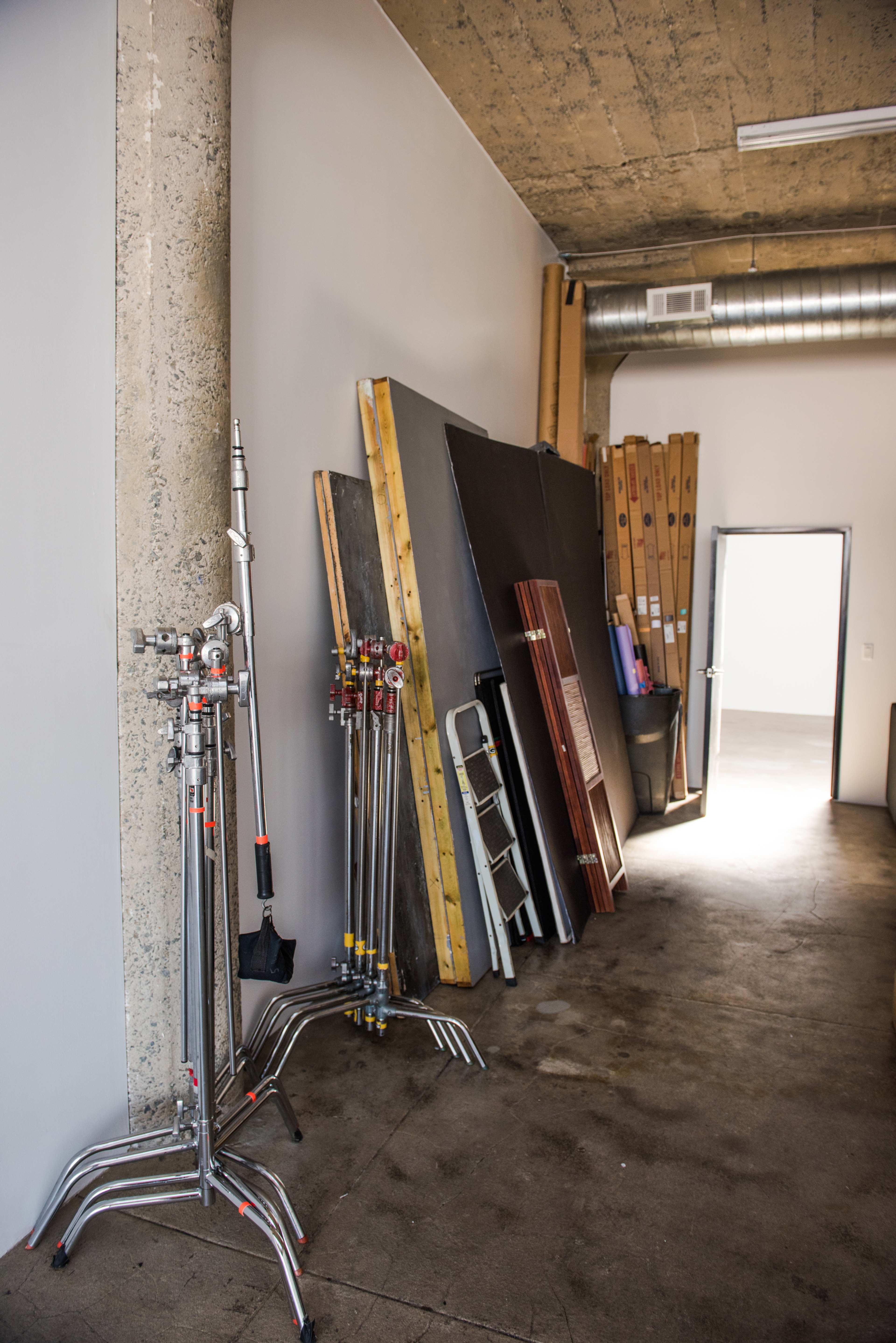 A storage area with lighting stands, wooden panels, and a ladder leaning against an interior wall.