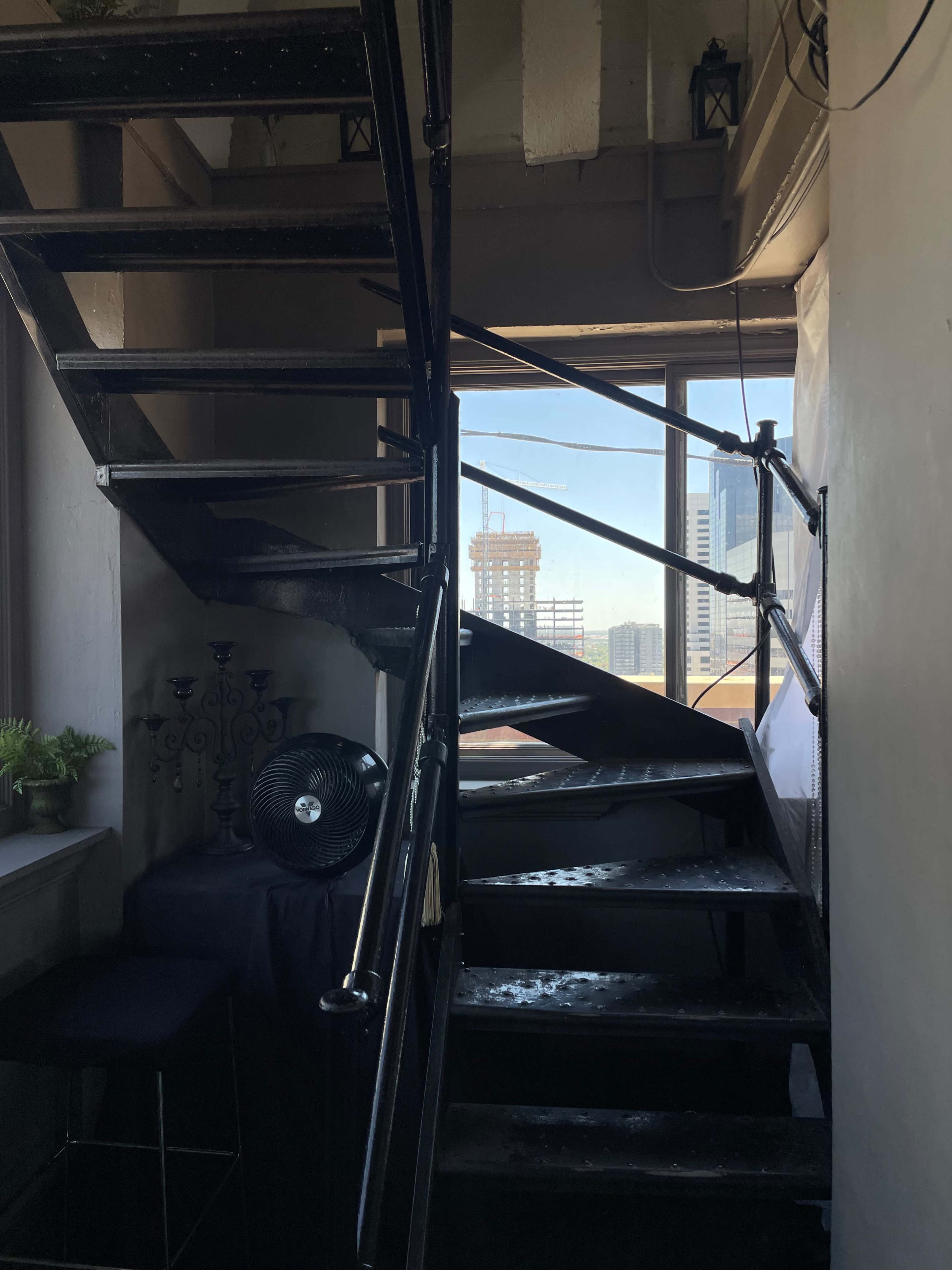 A winding metal staircase leads to a window with a view of a city skyline.