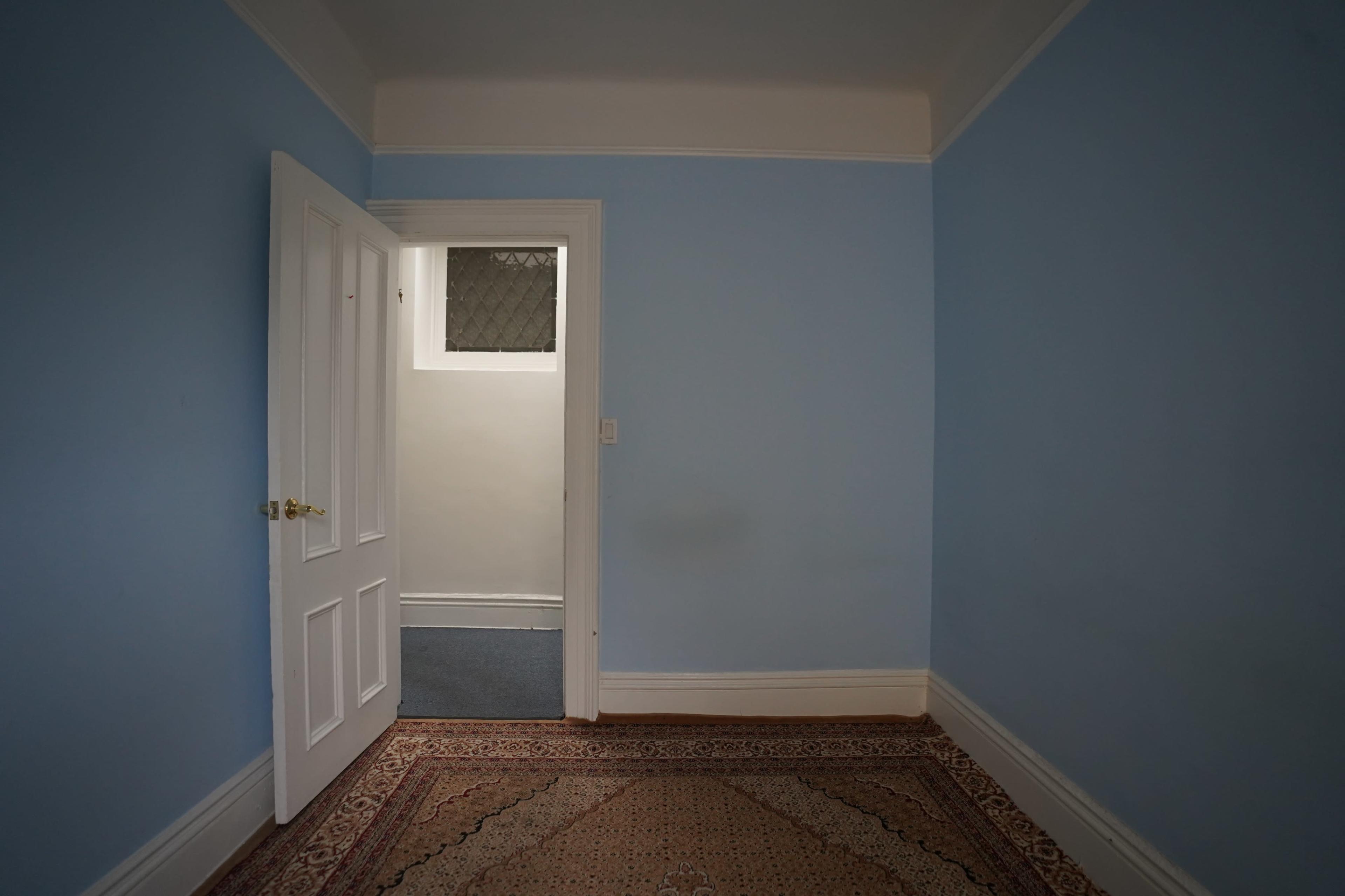 A light blue room with an open white door leading to a hallway and a patterned rug on the floor.