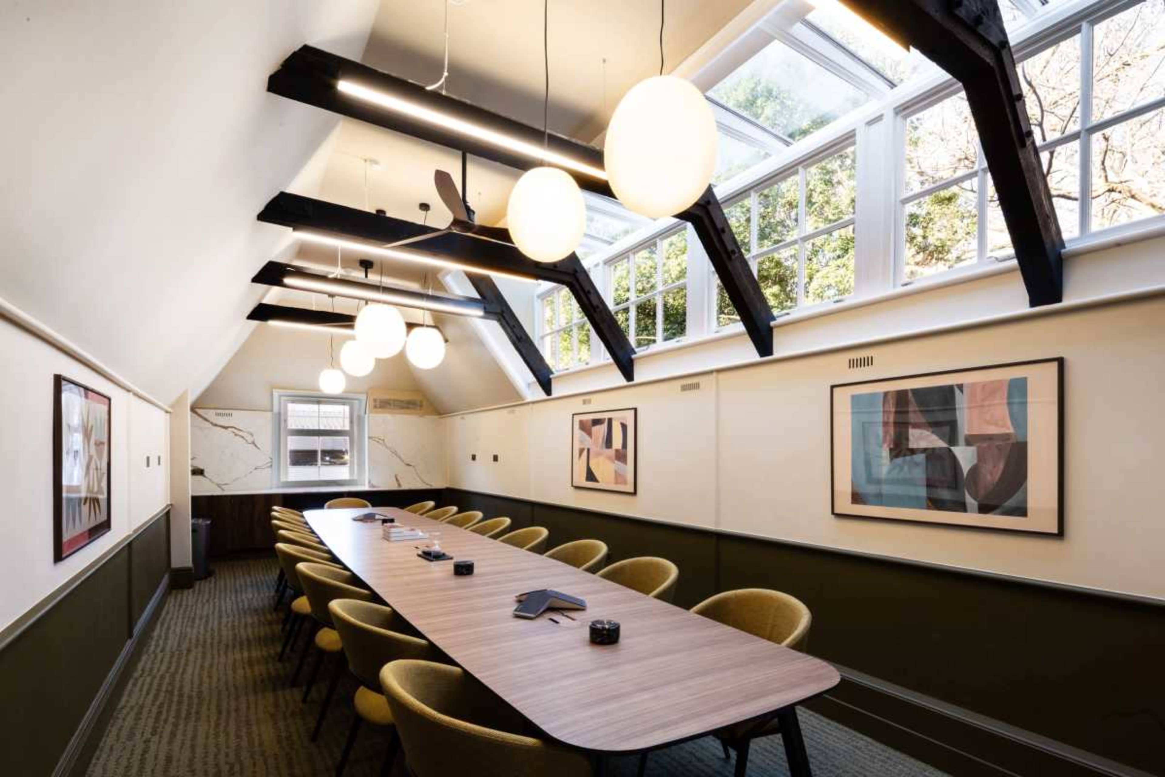 The image shows a modern conference room with a long rectangular table, yellow chairs, and large windows that allow natural light to illuminate the space.