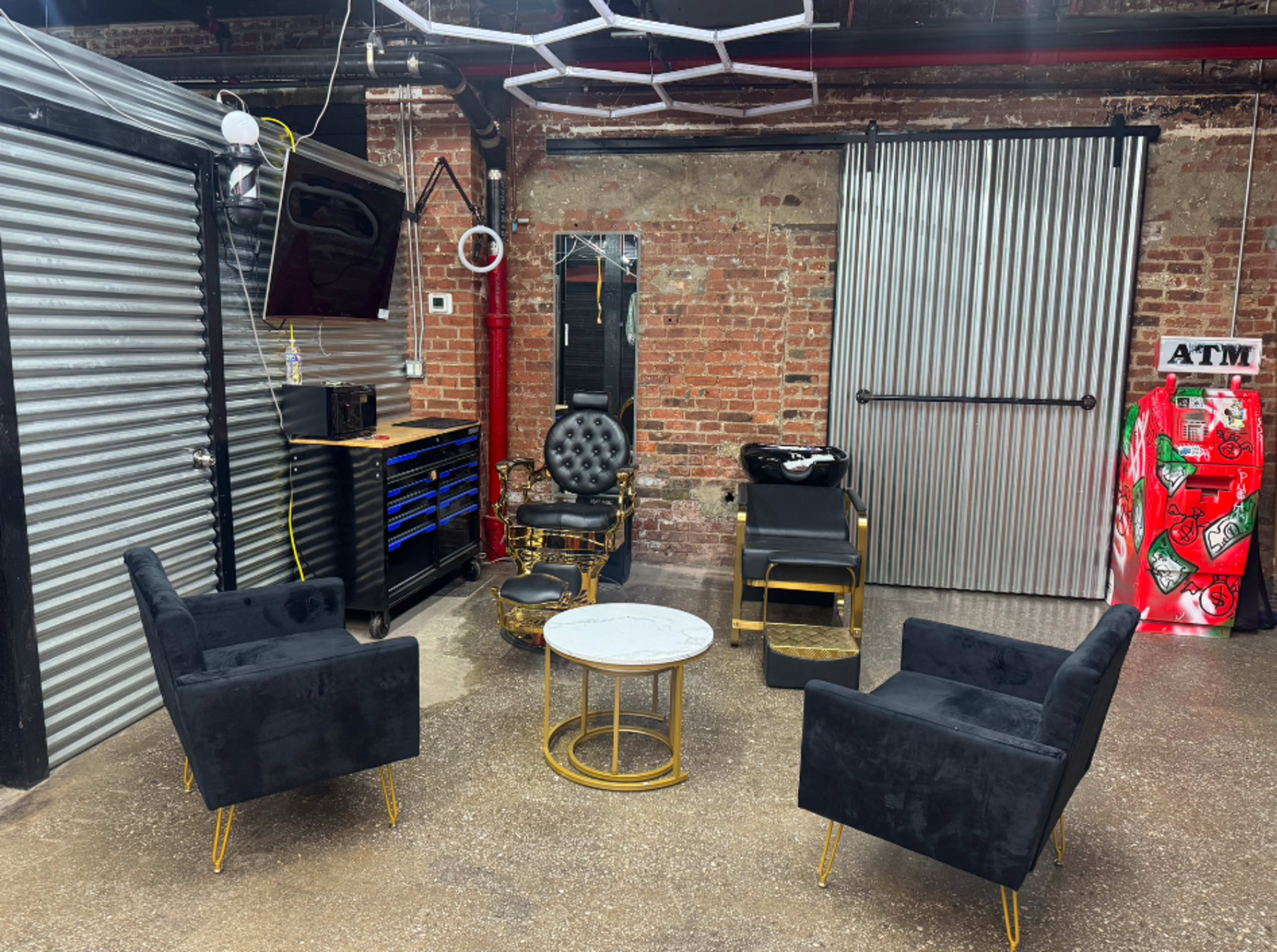 The image shows a modern industrial-style room with exposed brick walls, featuring a seating area with four black chairs surrounding a circular table, and a wall-mounted TV.