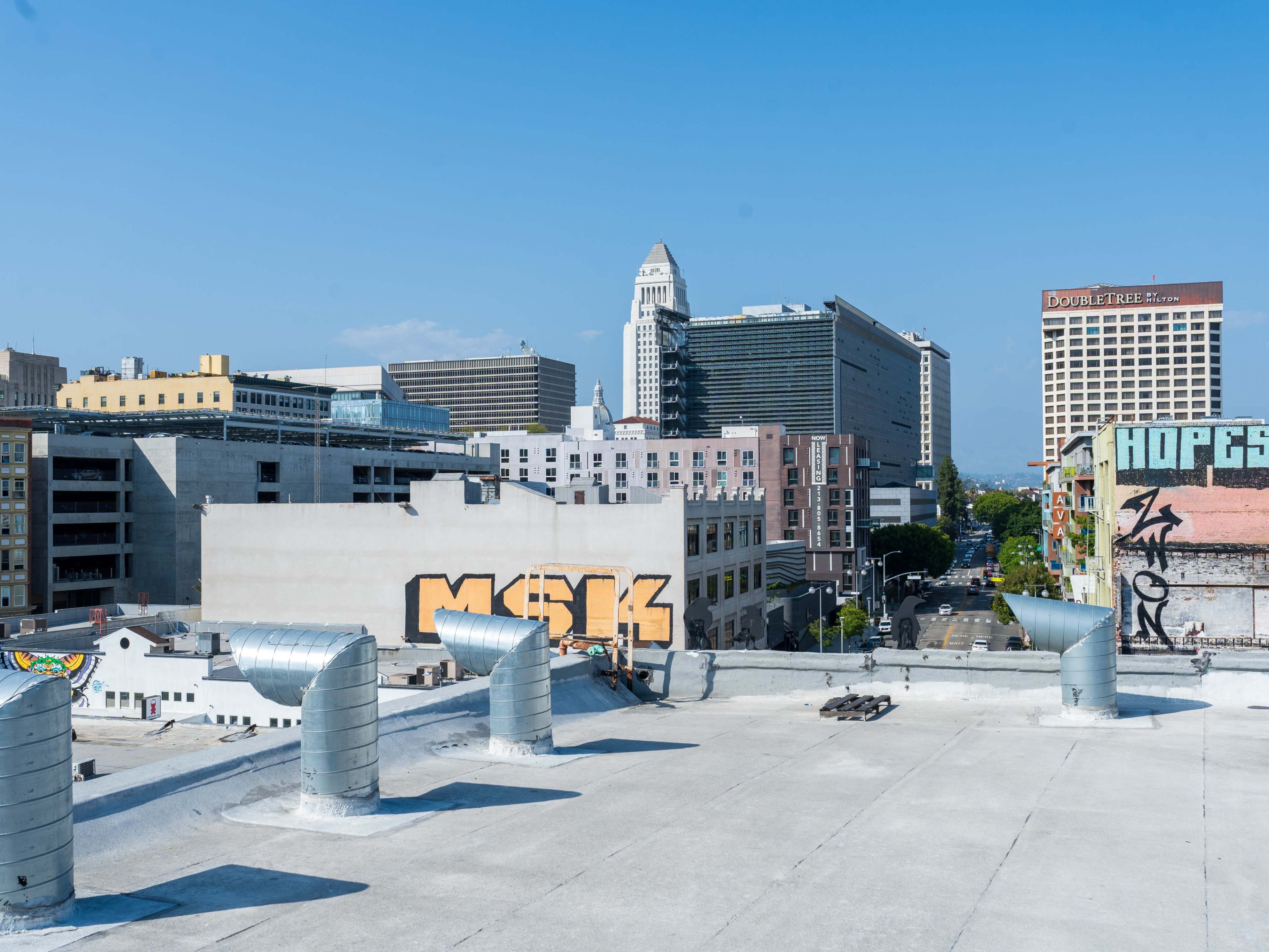 The image shows a rooftop view of a cityscape with several buildings, including skyscrapers and graffiti on the walls.
