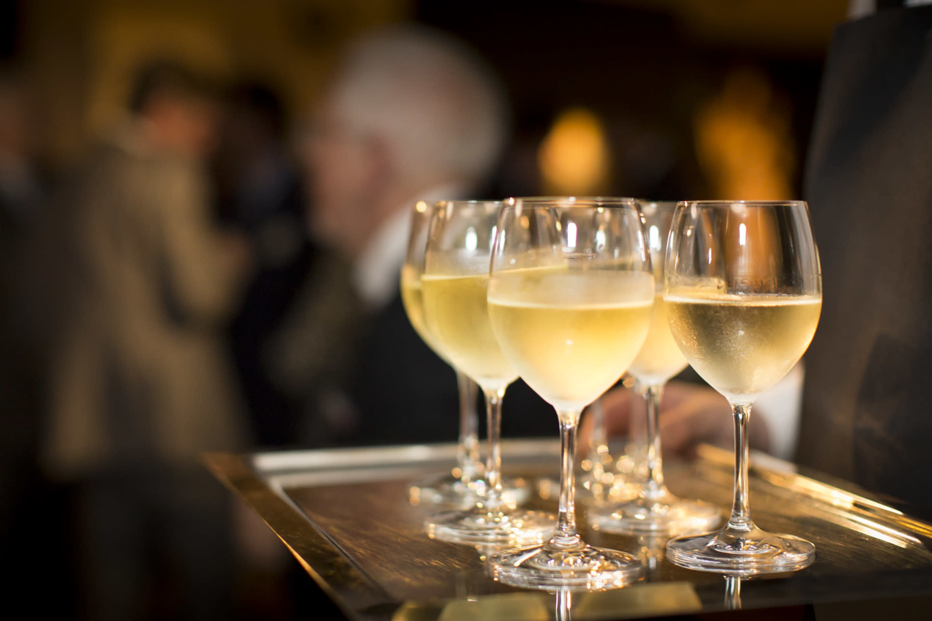 A tray holds several glasses of white wine at a social event.