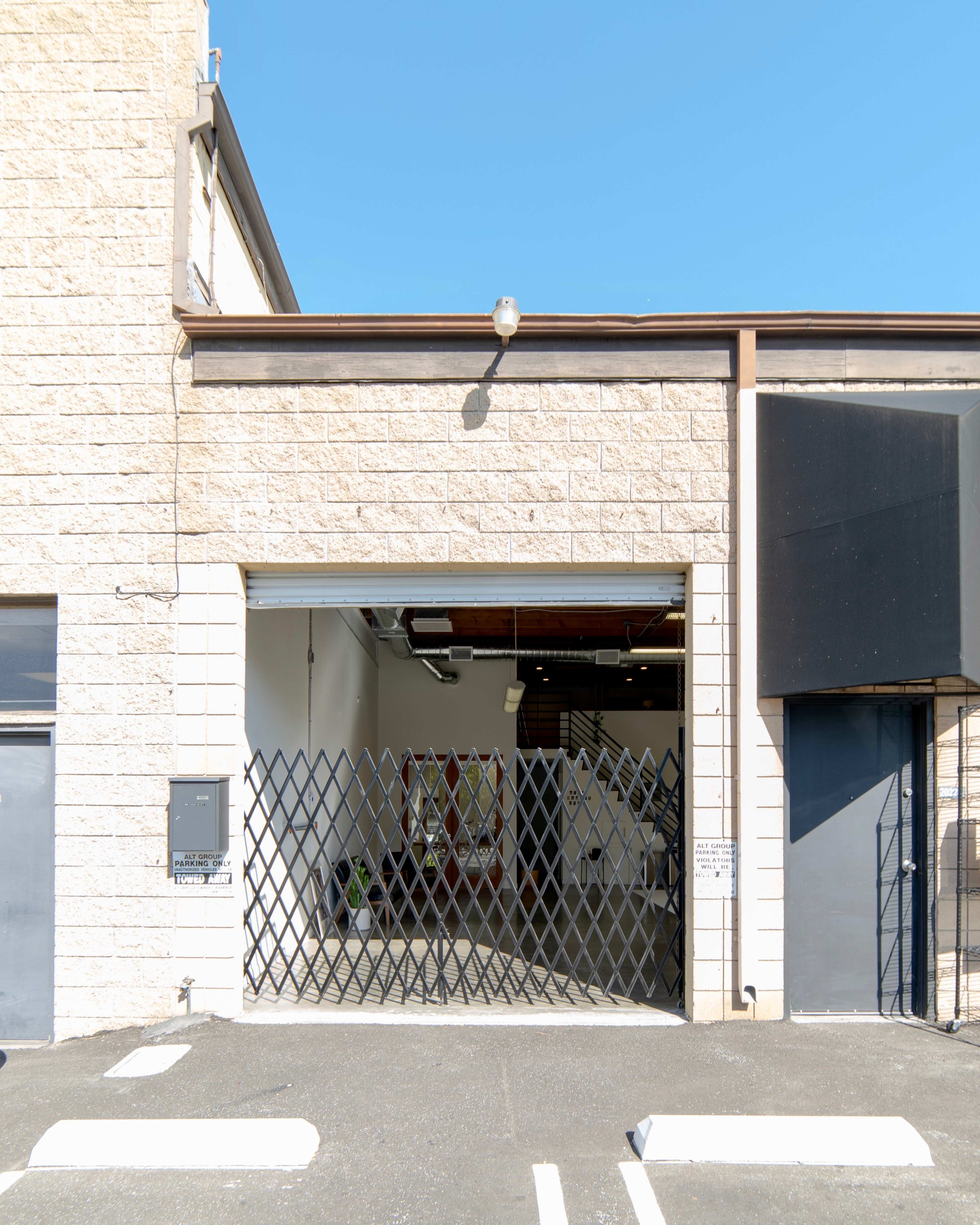 A large industrial garage door is partially open, revealing an empty interior space with a black metal security grille across the entrance.