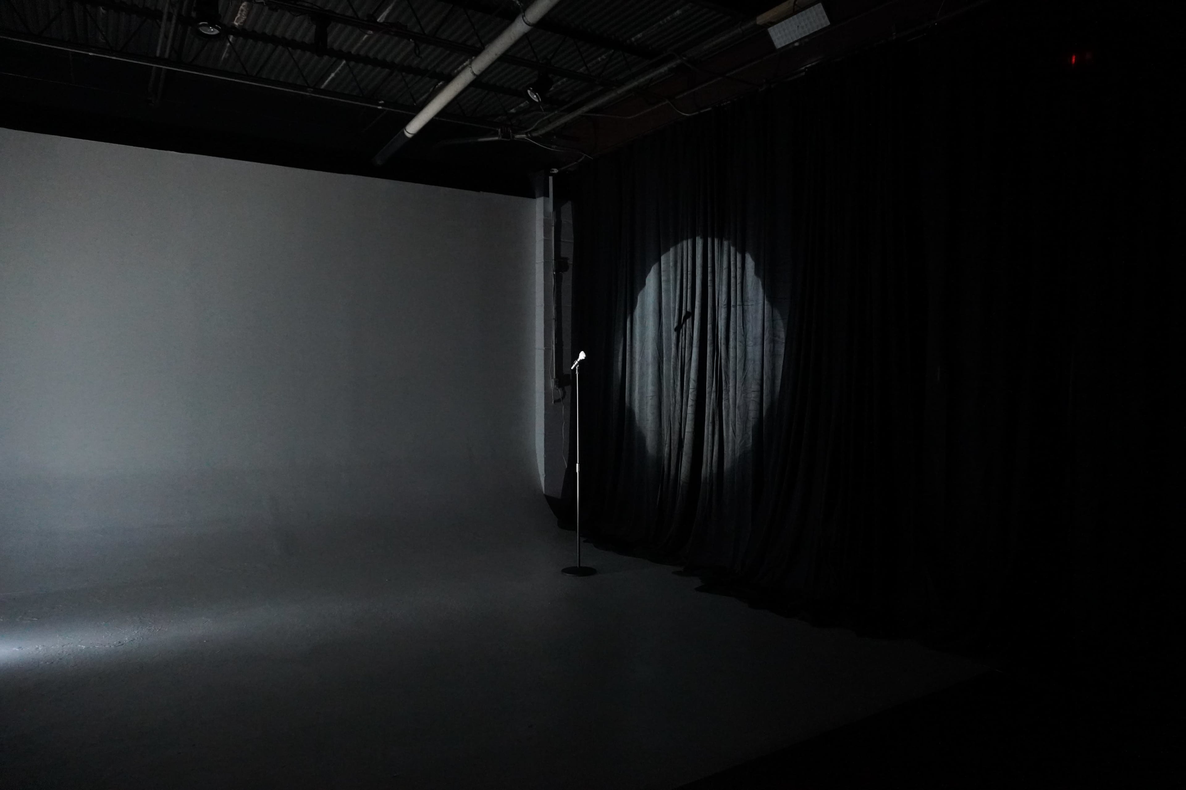 A spotlight illuminates a microphone stand on a sparse stage set against a black curtain.