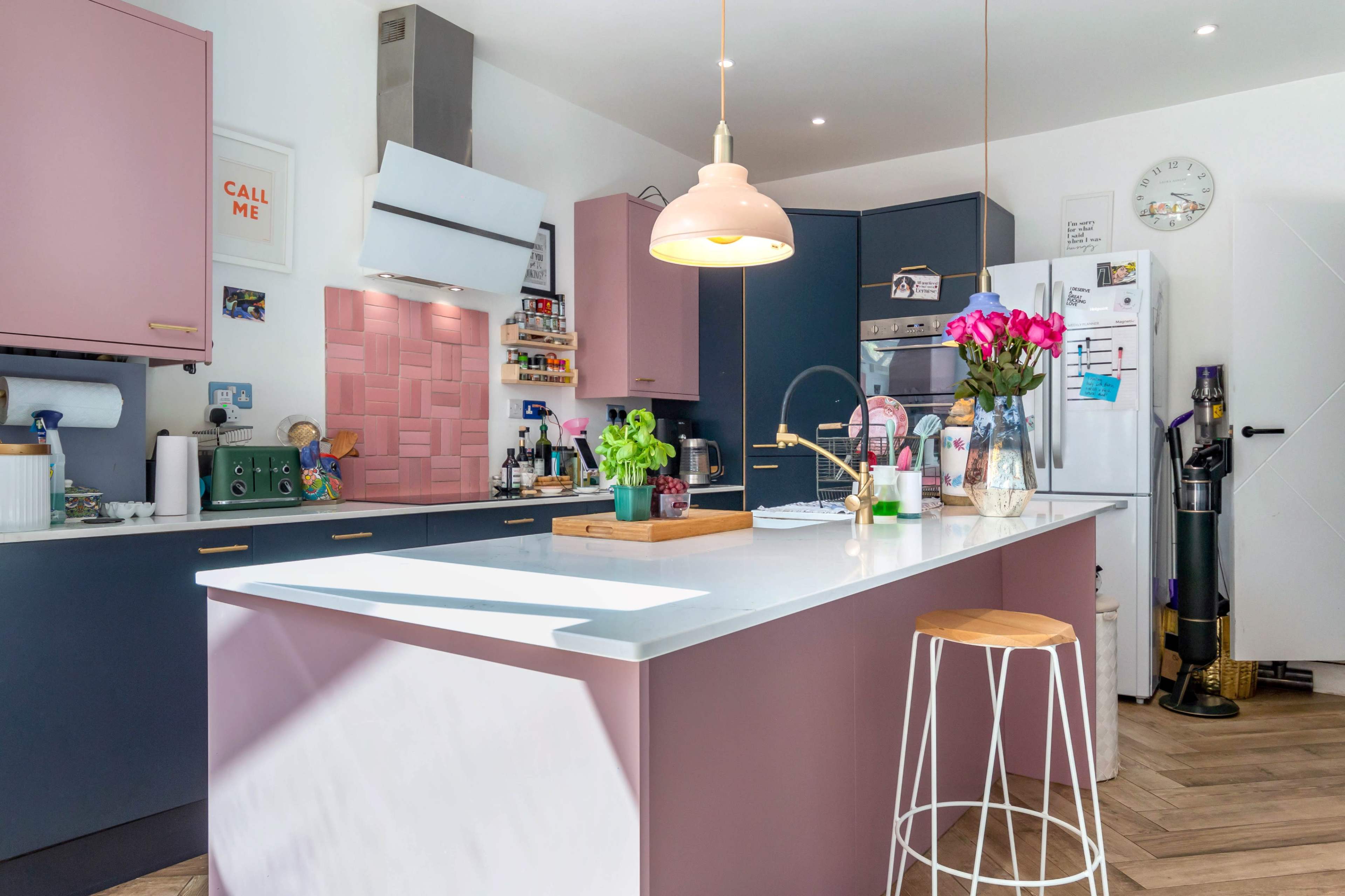 The kitchen features a modern design with a central island, pink and blue cabinetry, and a vase of flowers on the countertop.
