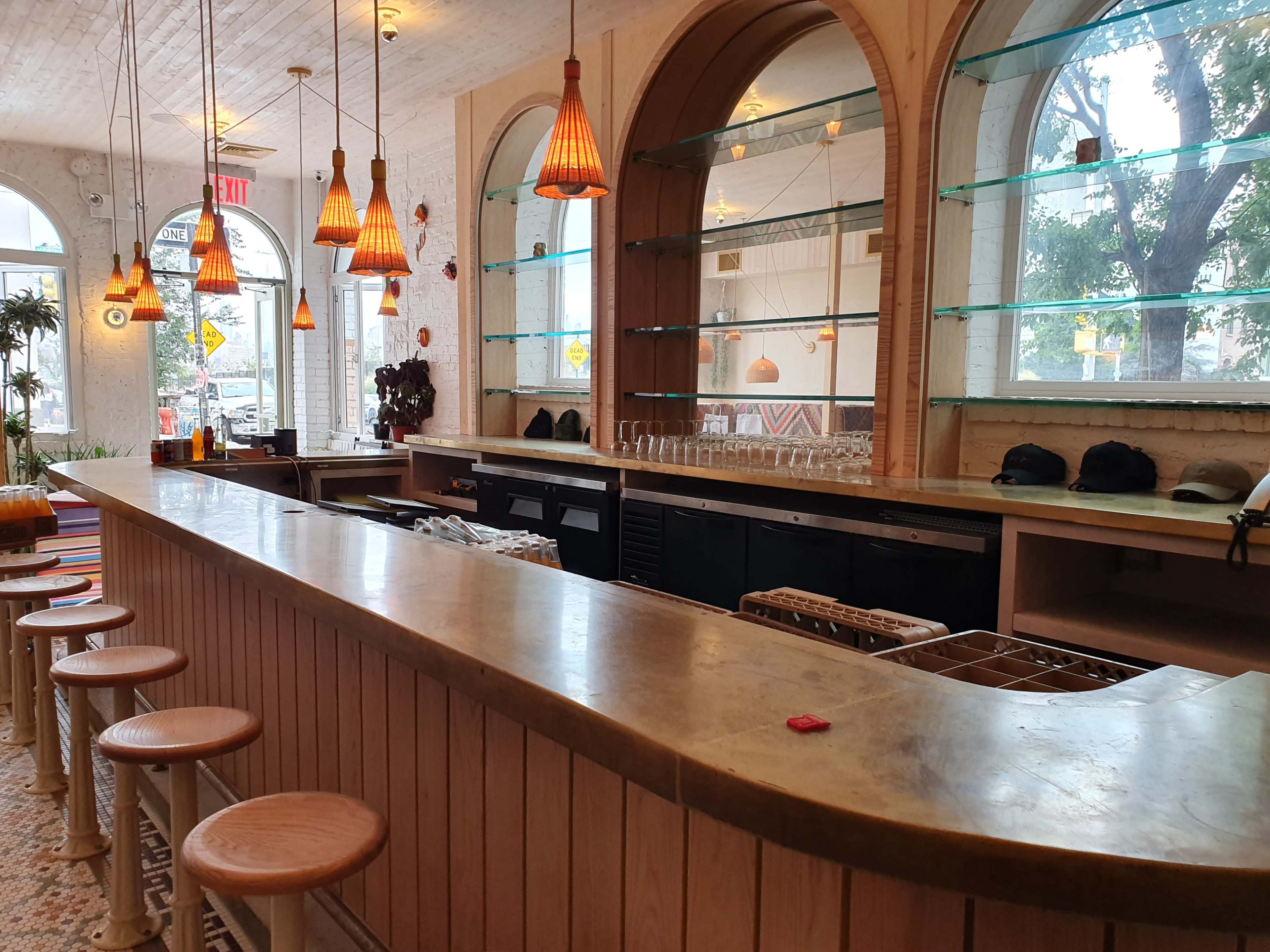 A wooden bar area with round stools, illuminated pendant lights, and large arched windows.