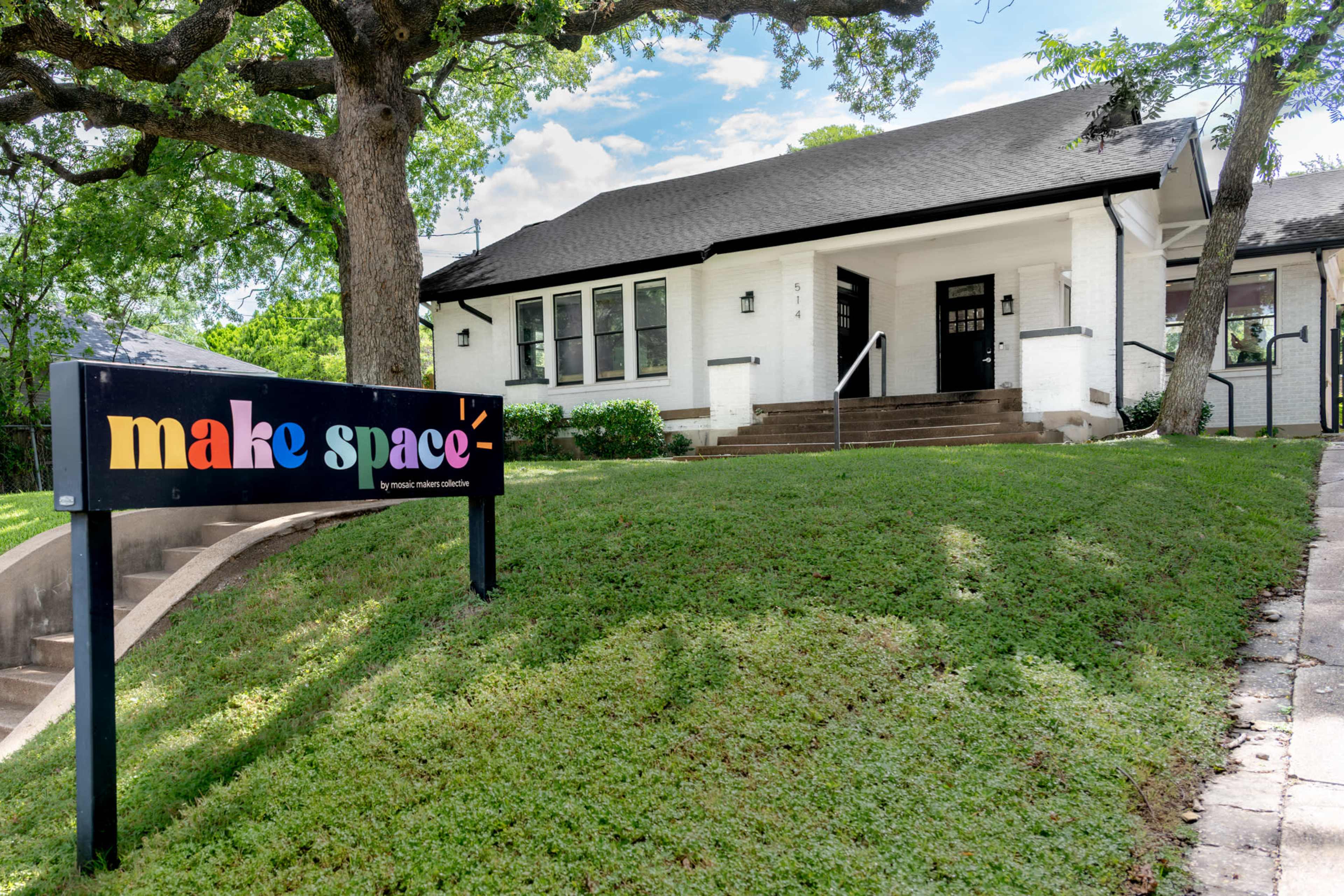 The image shows a white building with a sloped lawn and a colorful sign that reads "make space."