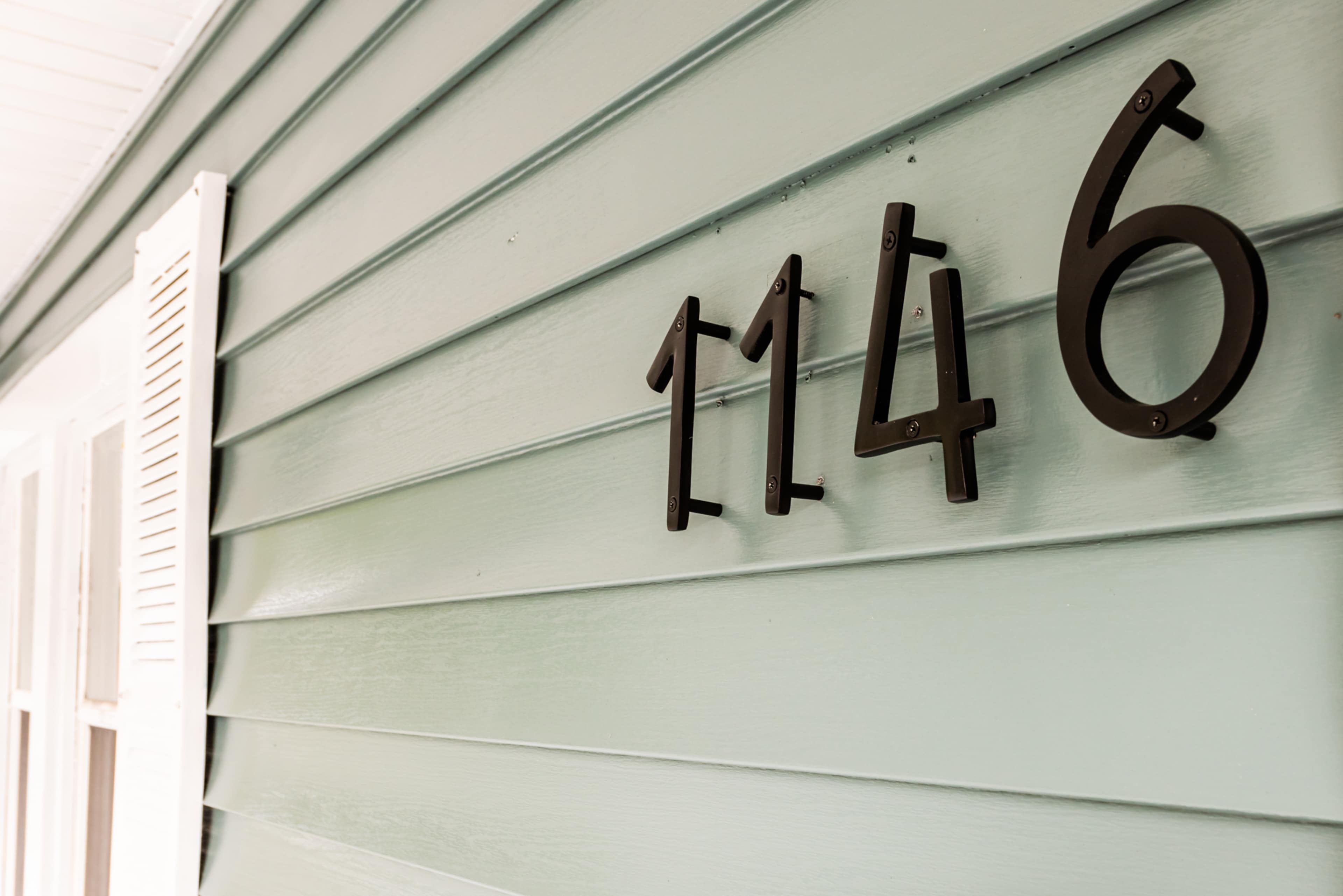 The house number "1146" displayed in black metal on a light green wooden wall.