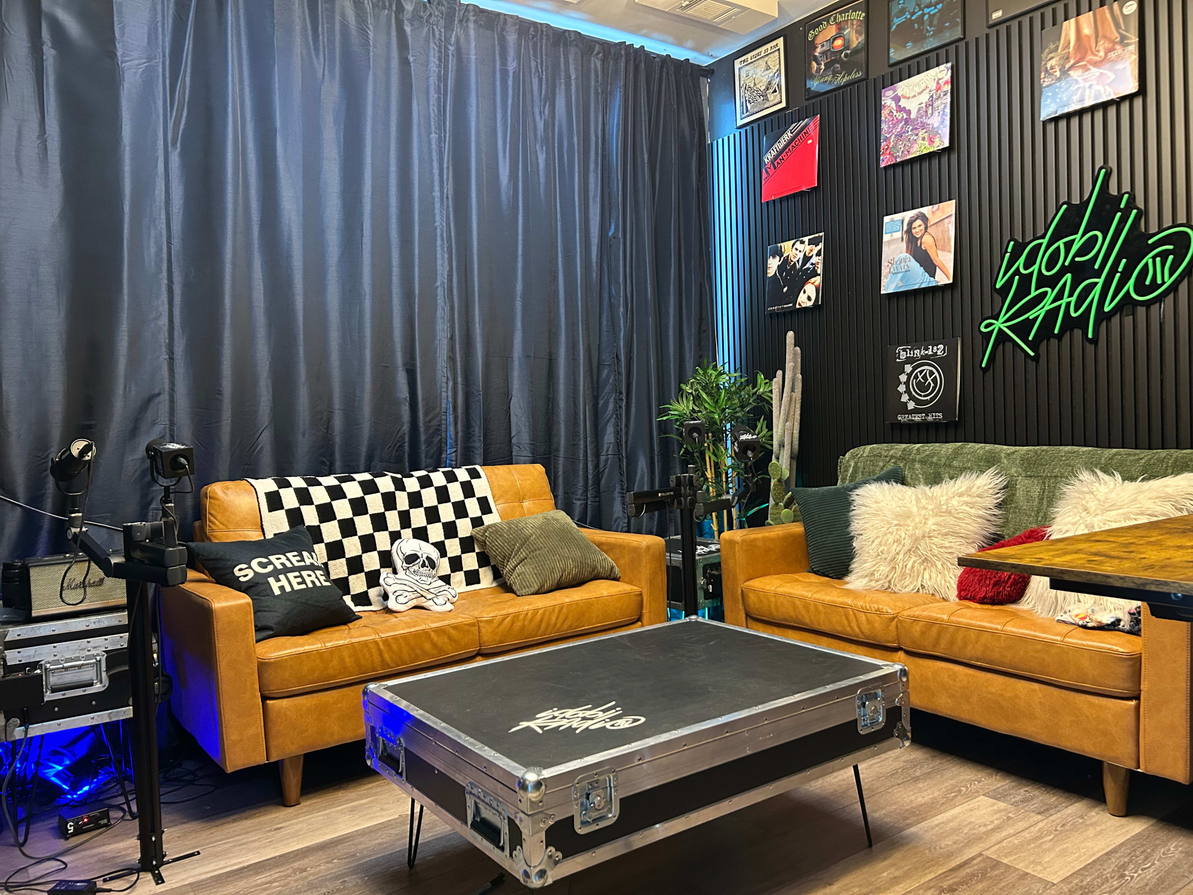 The image shows a modern lounge area with two brown sofas, a coffee table, and a backdrop of black curtains and decorative wall art.