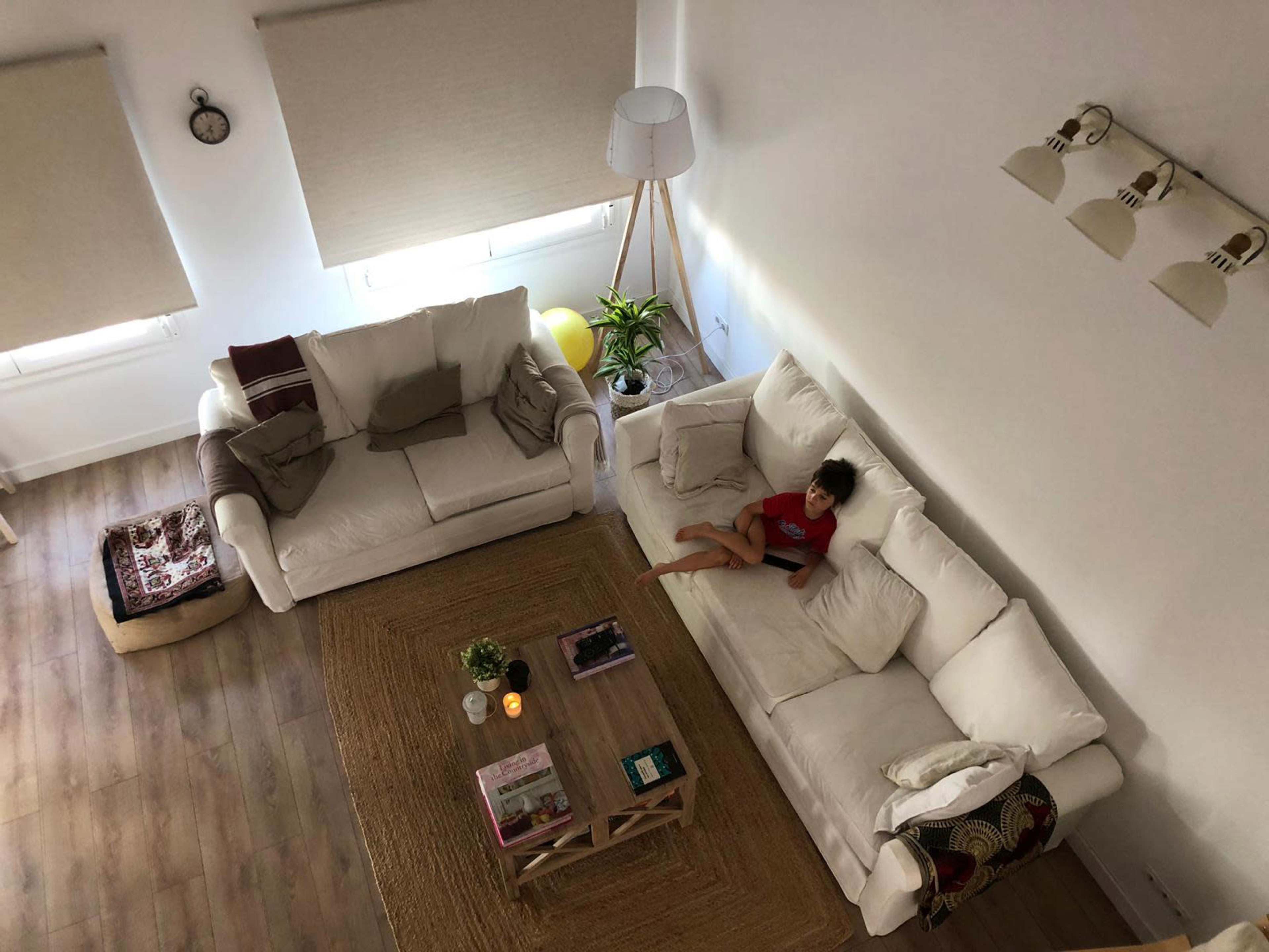 A child sits on a white sofa in a bright, modern living room with a large rug and a coffee table.