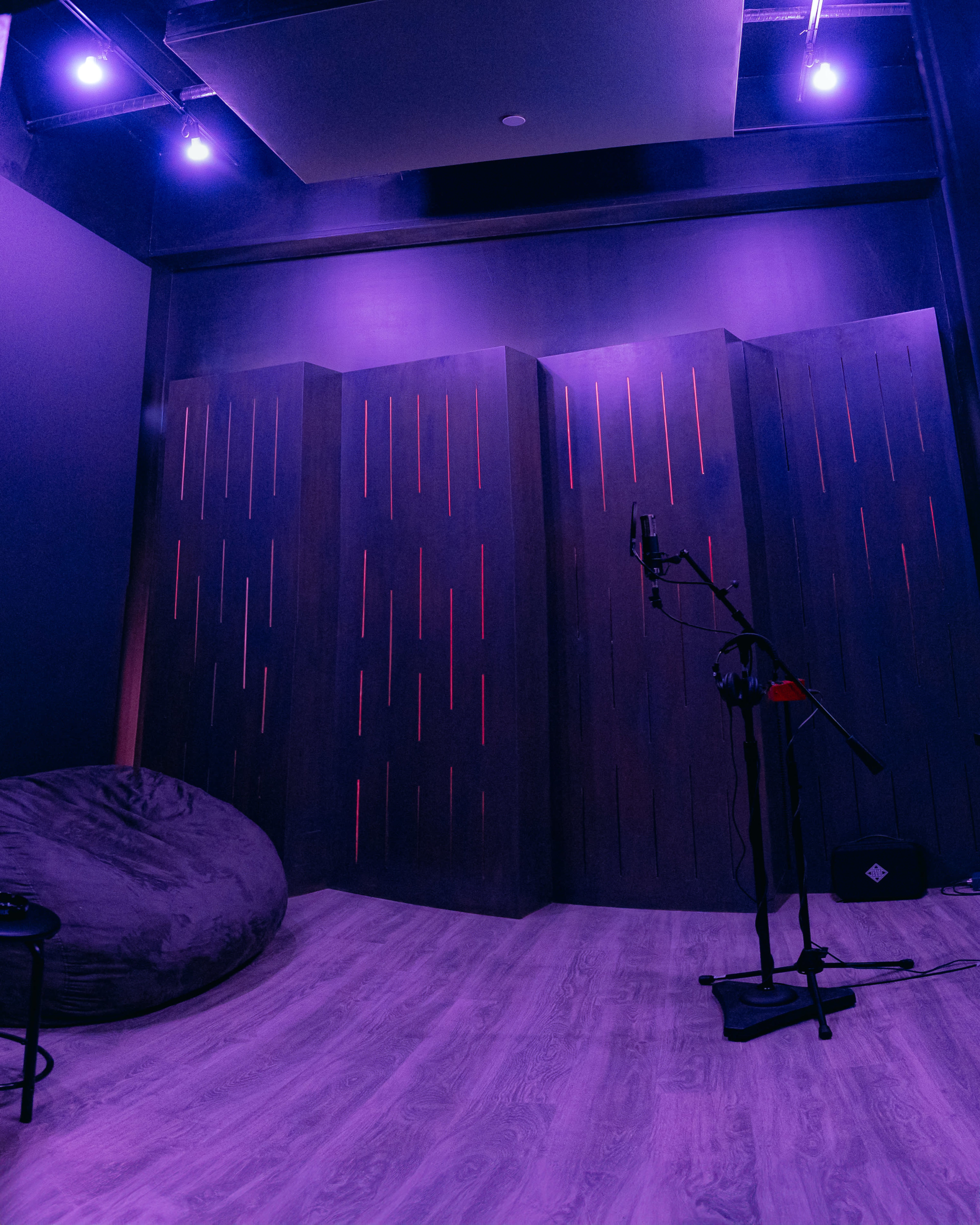 The image shows a dark recording studio with purple lighting, a microphone on a stand, and a large bean bag.