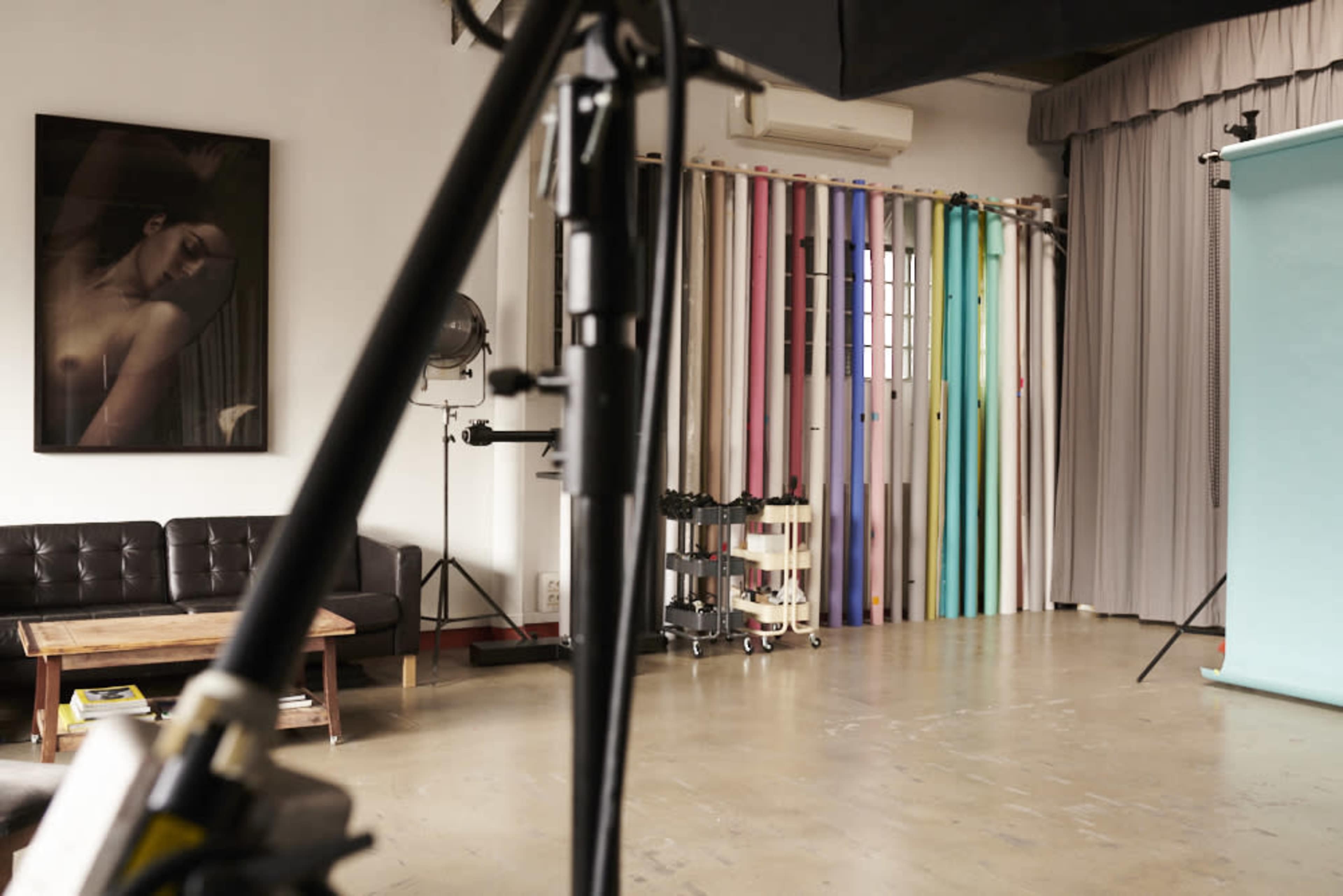 A photography studio with a black sofa, a large portrait on the wall, and a backdrop holder featuring various colored backdrops.