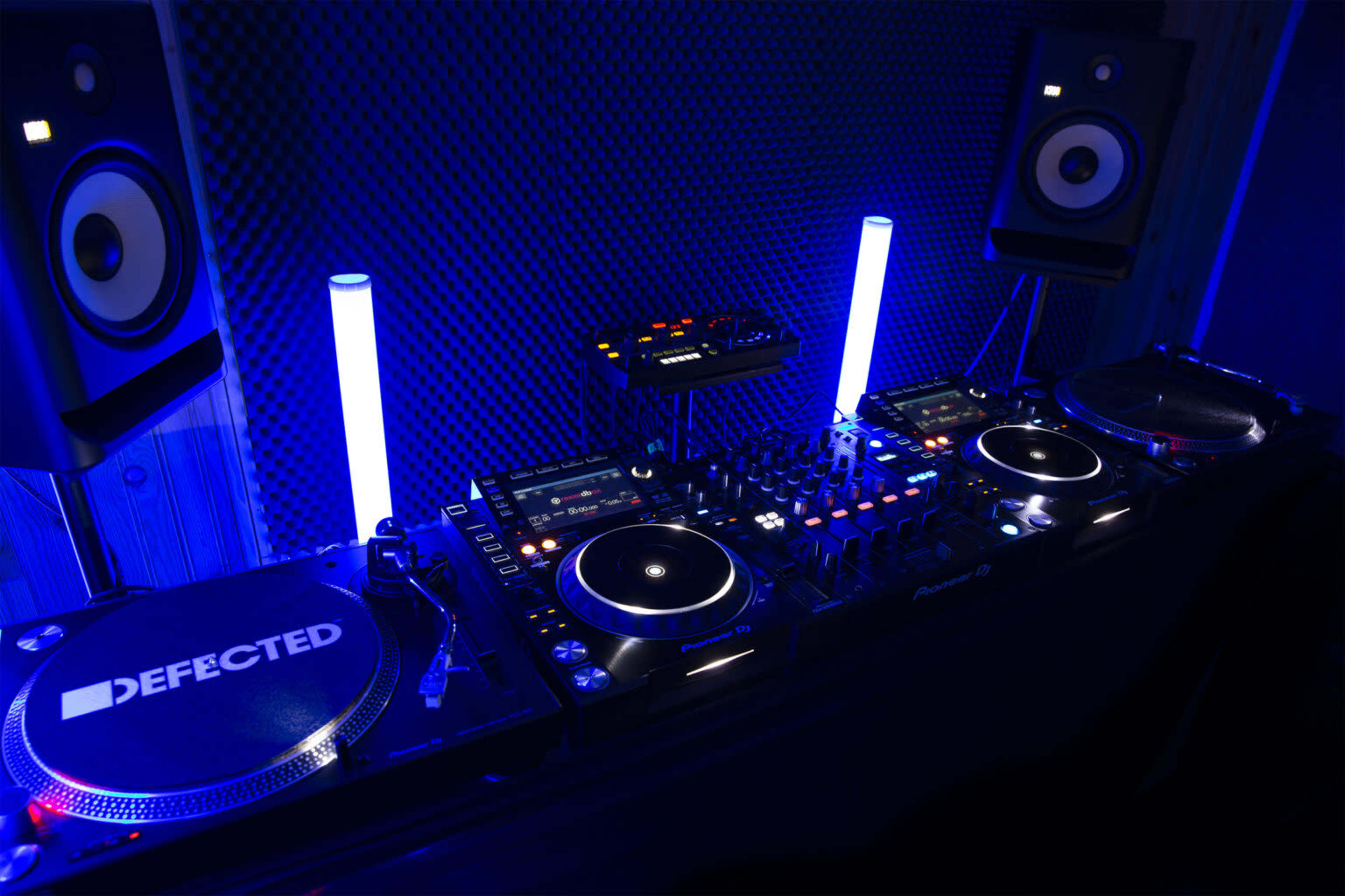 A DJ setup featuring turntables, a mixer, and studio monitors, all illuminated by blue lights.