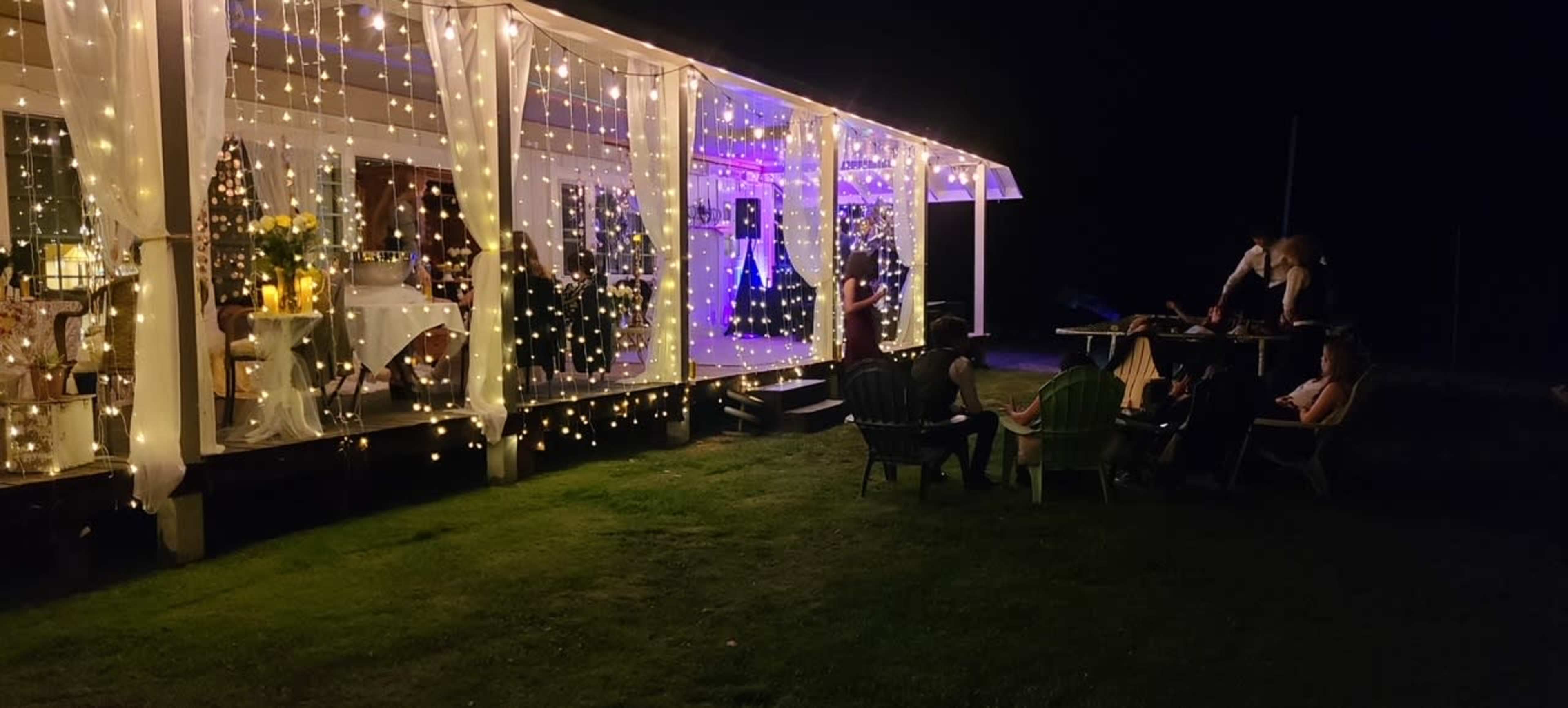 A decorated outdoor patio with string lights and people gathered around a table in the evening.