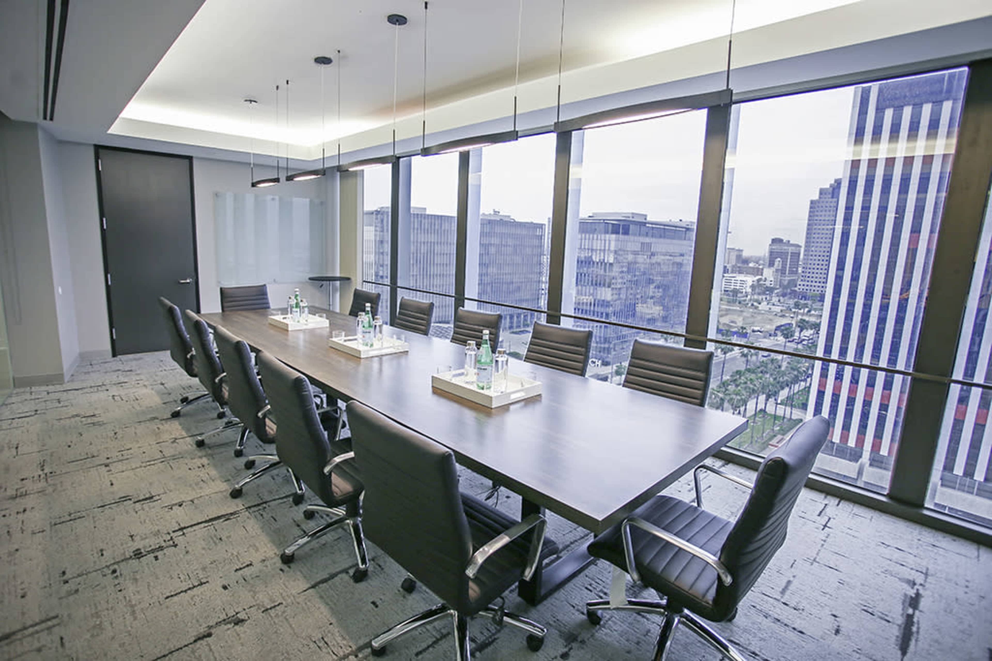 A modern conference room features a large table surrounded by ergonomic chairs, with panoramic city views through floor-to-ceiling windows.