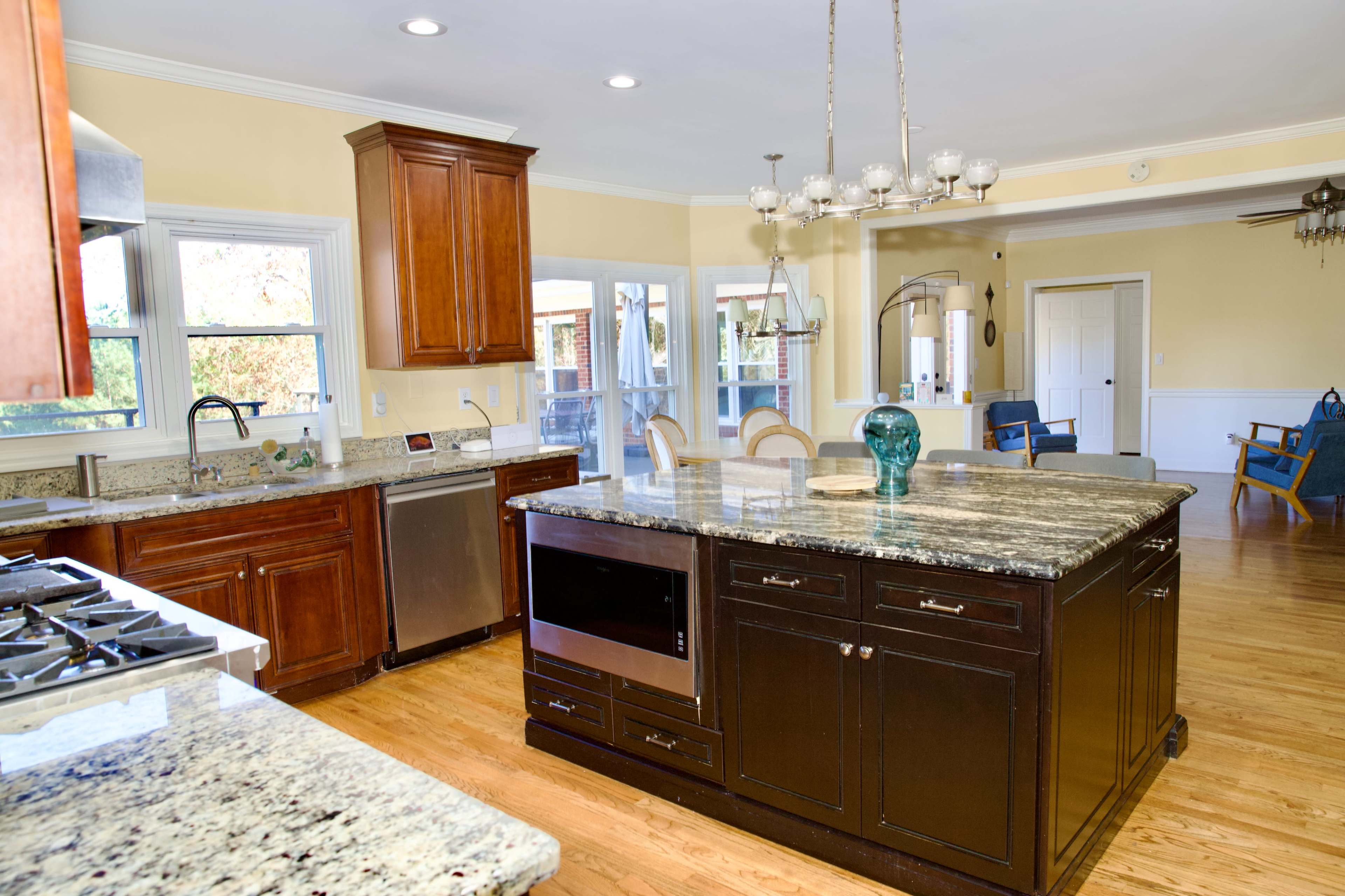 The image shows a spacious kitchen with wooden cabinets, a large granite island, and an open layout that connects to a dining area.