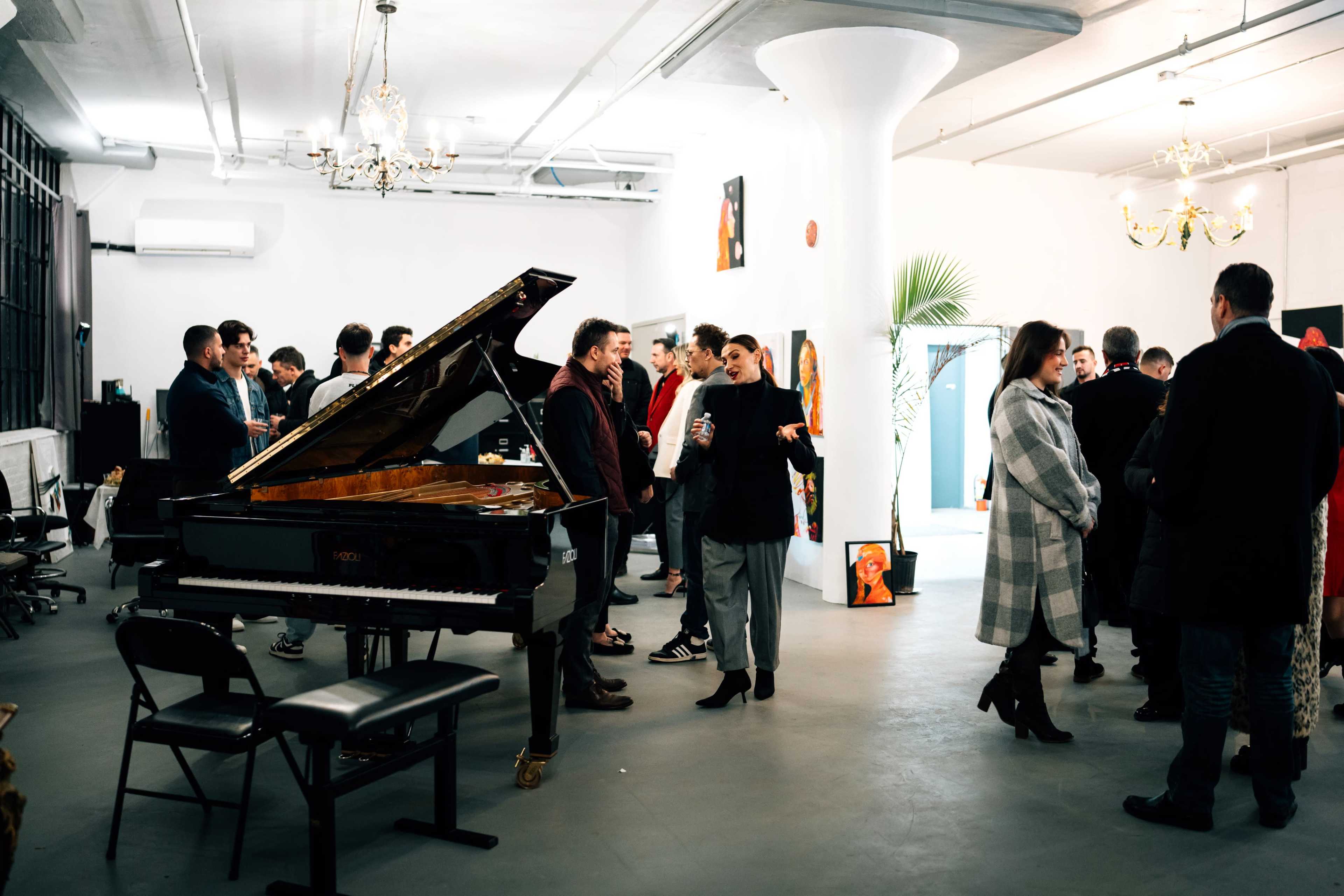 A group of people socialize in an art gallery with a grand piano in the foreground.