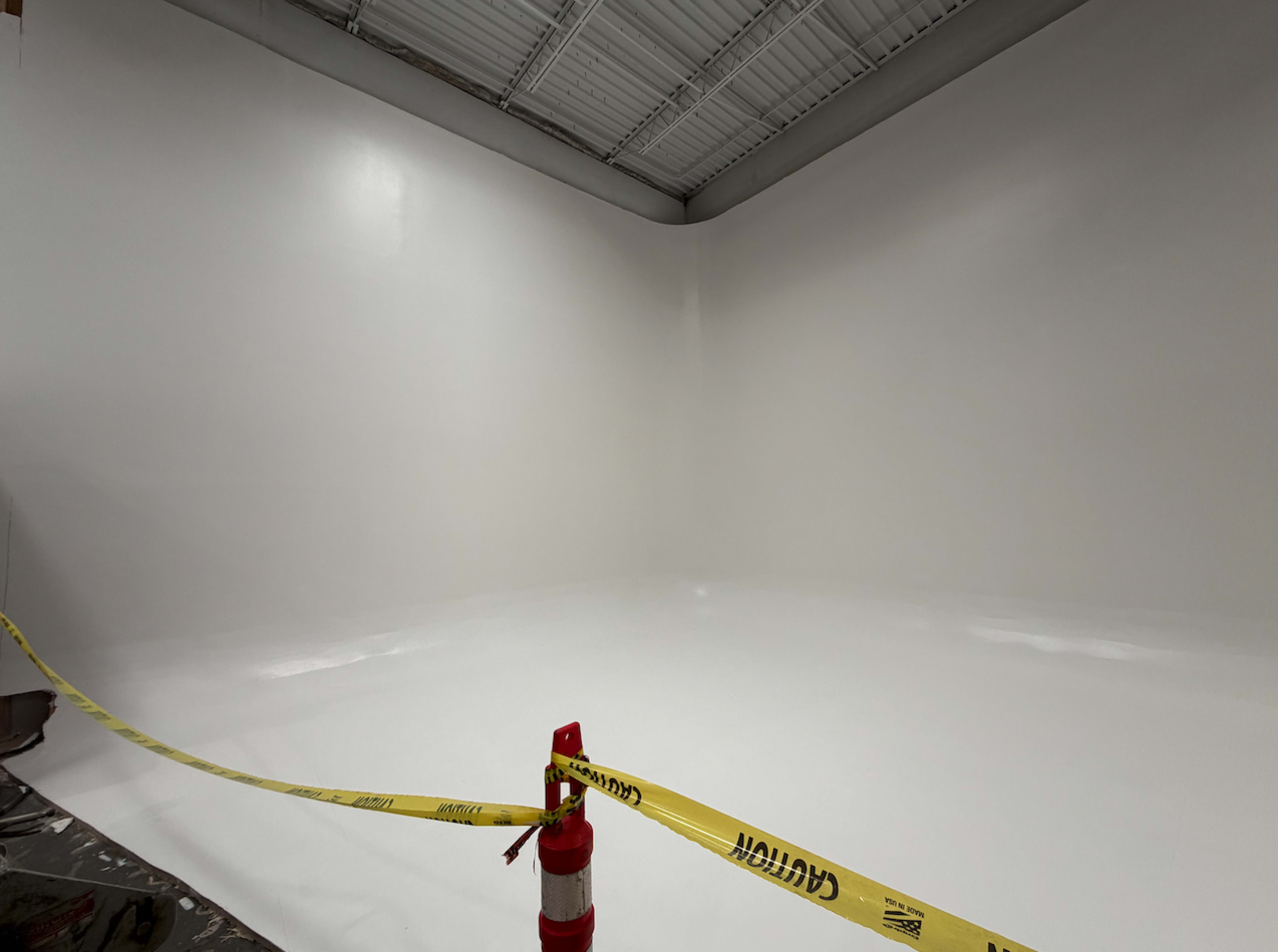 The image shows a clean, empty room with white walls and a shiny white floor, marked off with caution tape.