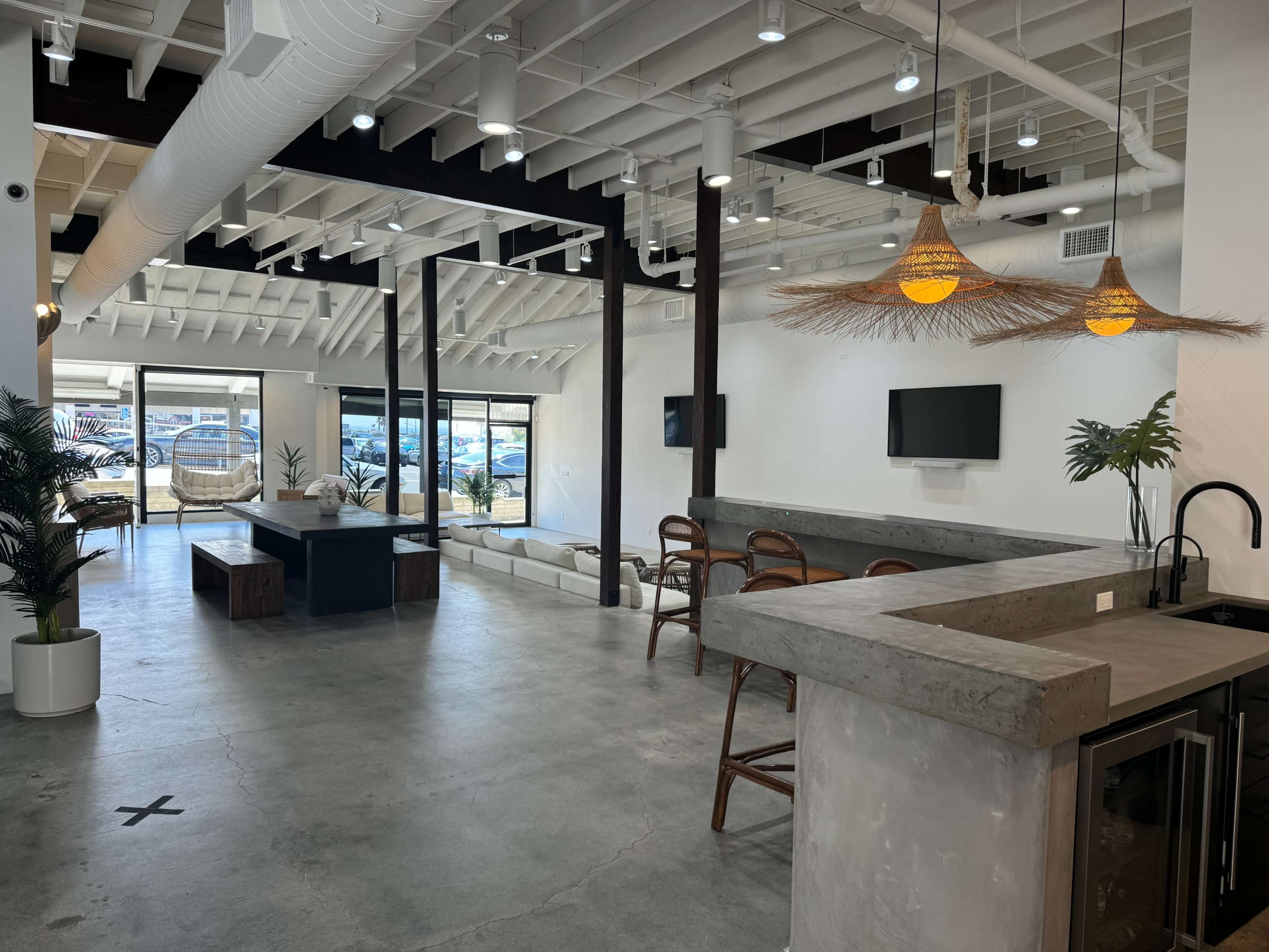 A modern interior space featuring concrete floors, wooden beams, seating areas, and a bar counter with high chairs.