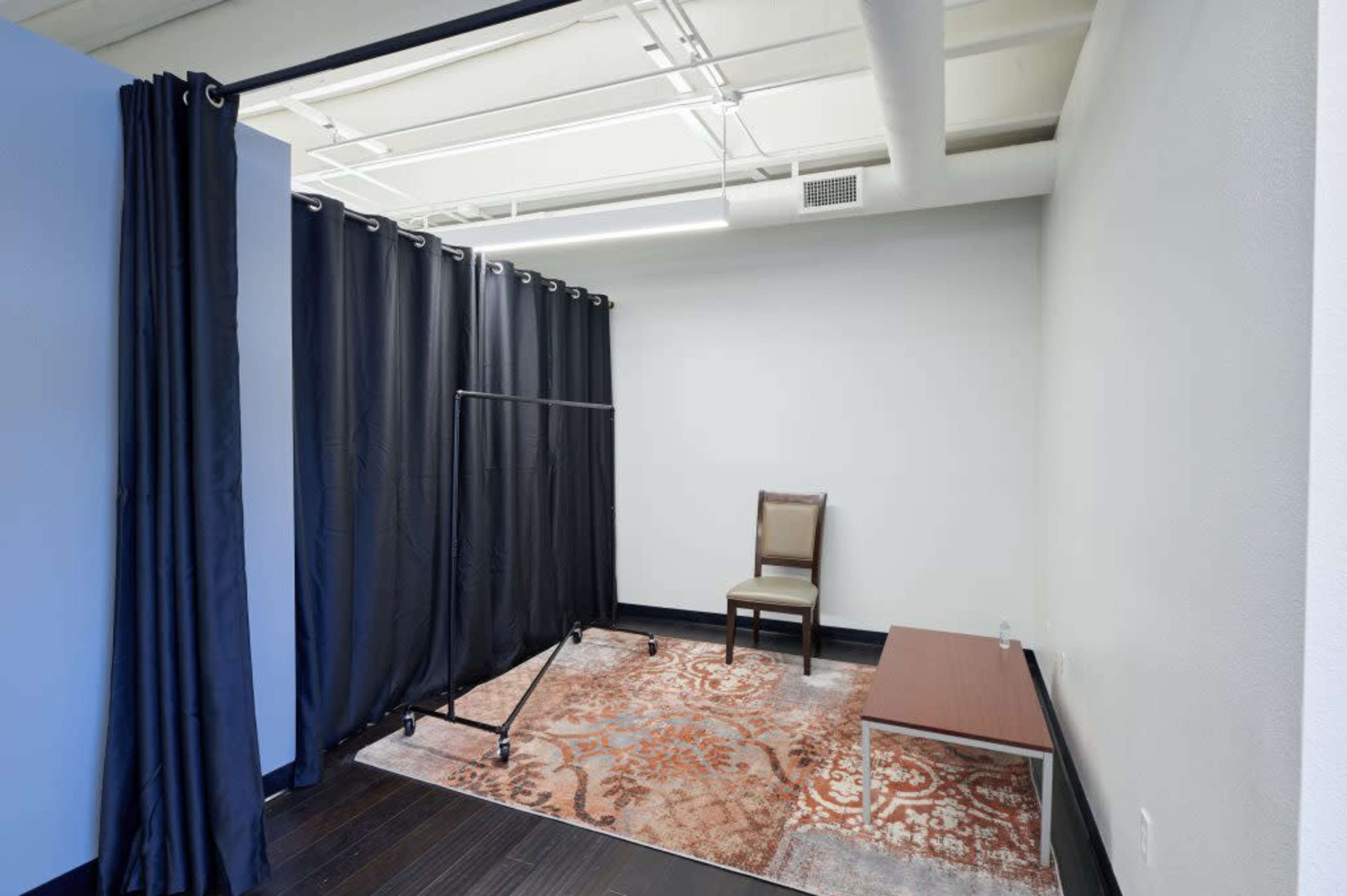 A small, minimally furnished room features a single chair, a table, and a large curtain dividing the space.