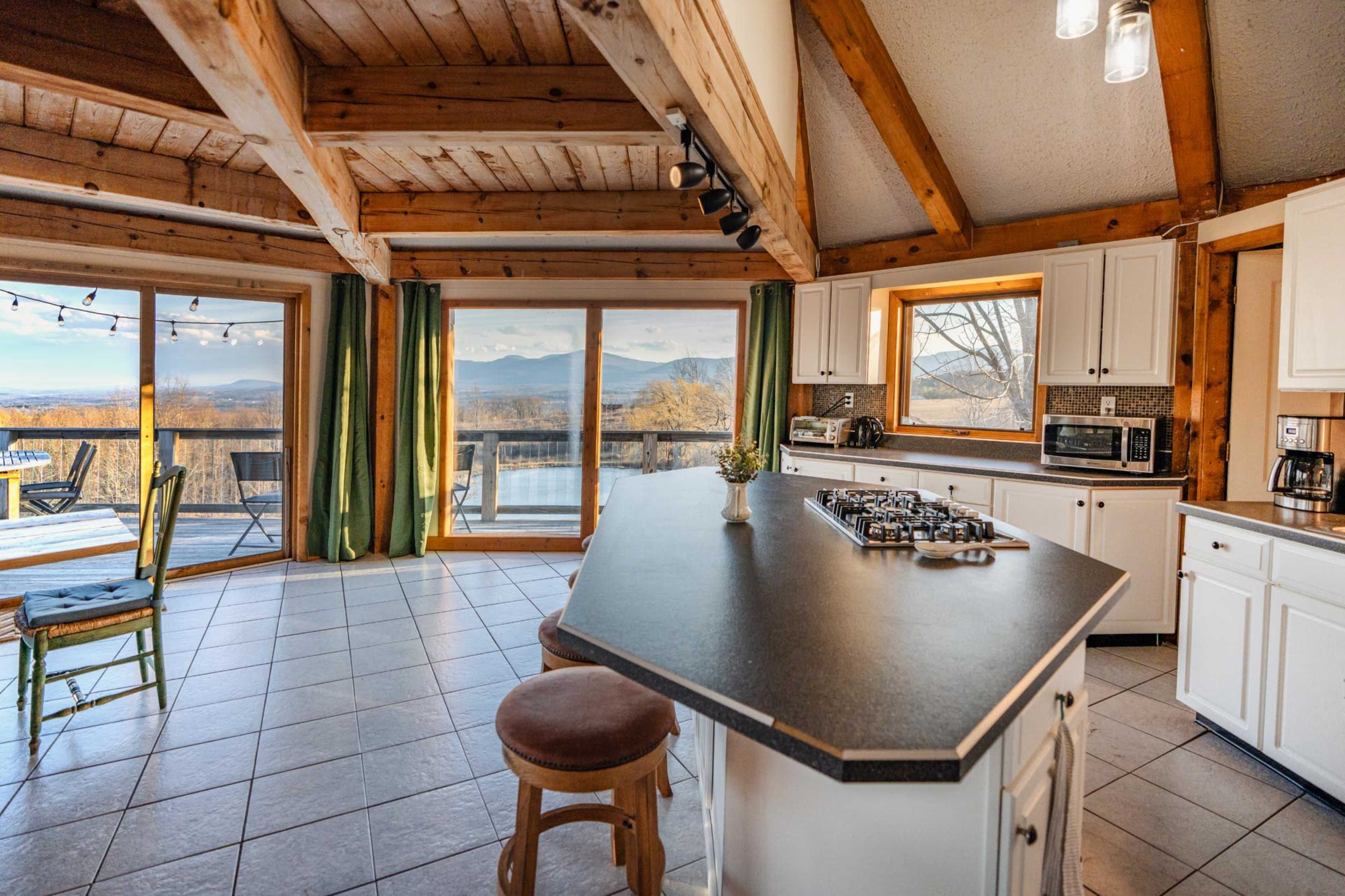 A spacious kitchen features a central island with a stovetop and has large windows that offer a view of the surrounding mountains.