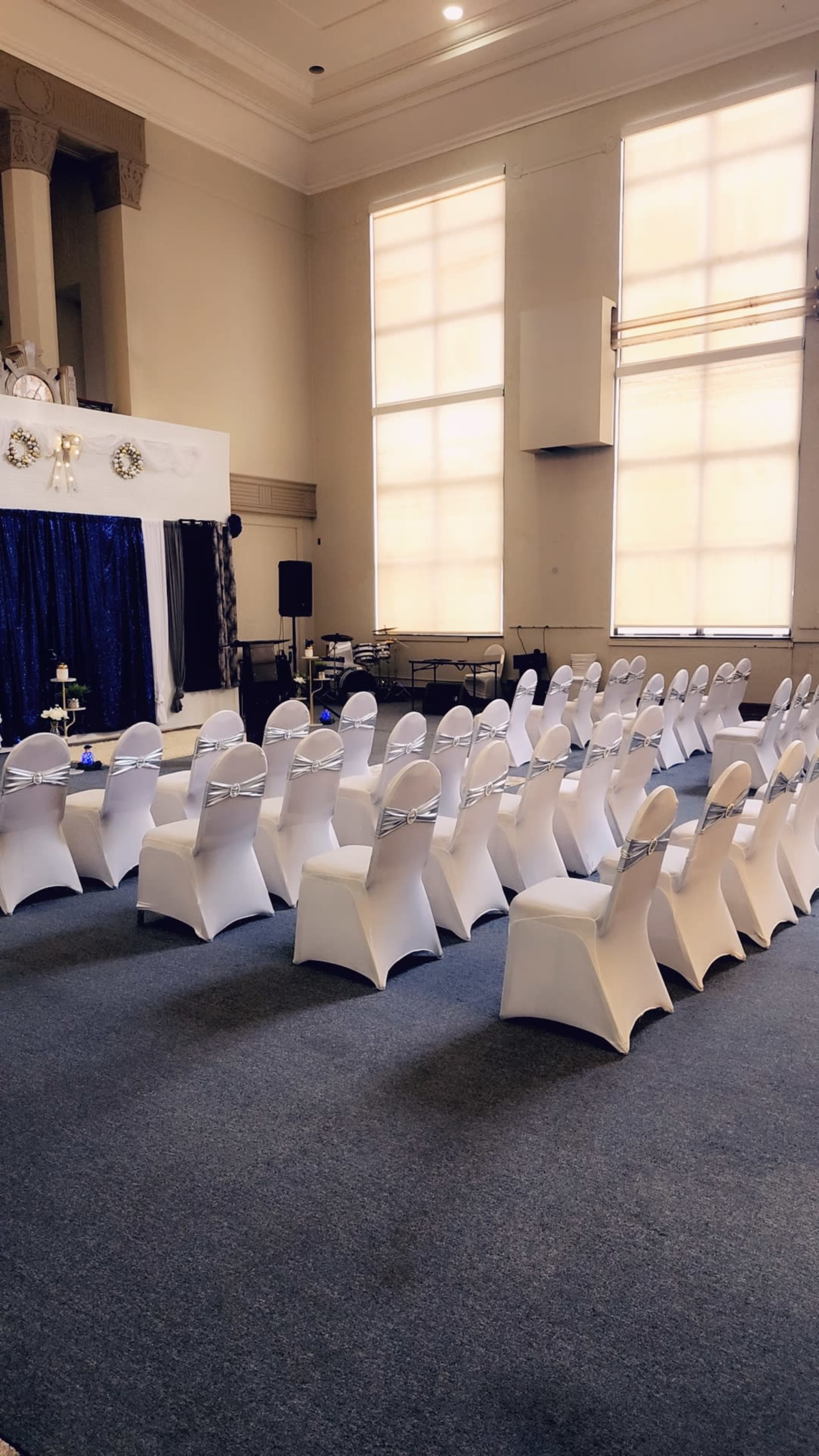 A formal event space is arranged with rows of white-covered chairs facing a decorated stage.