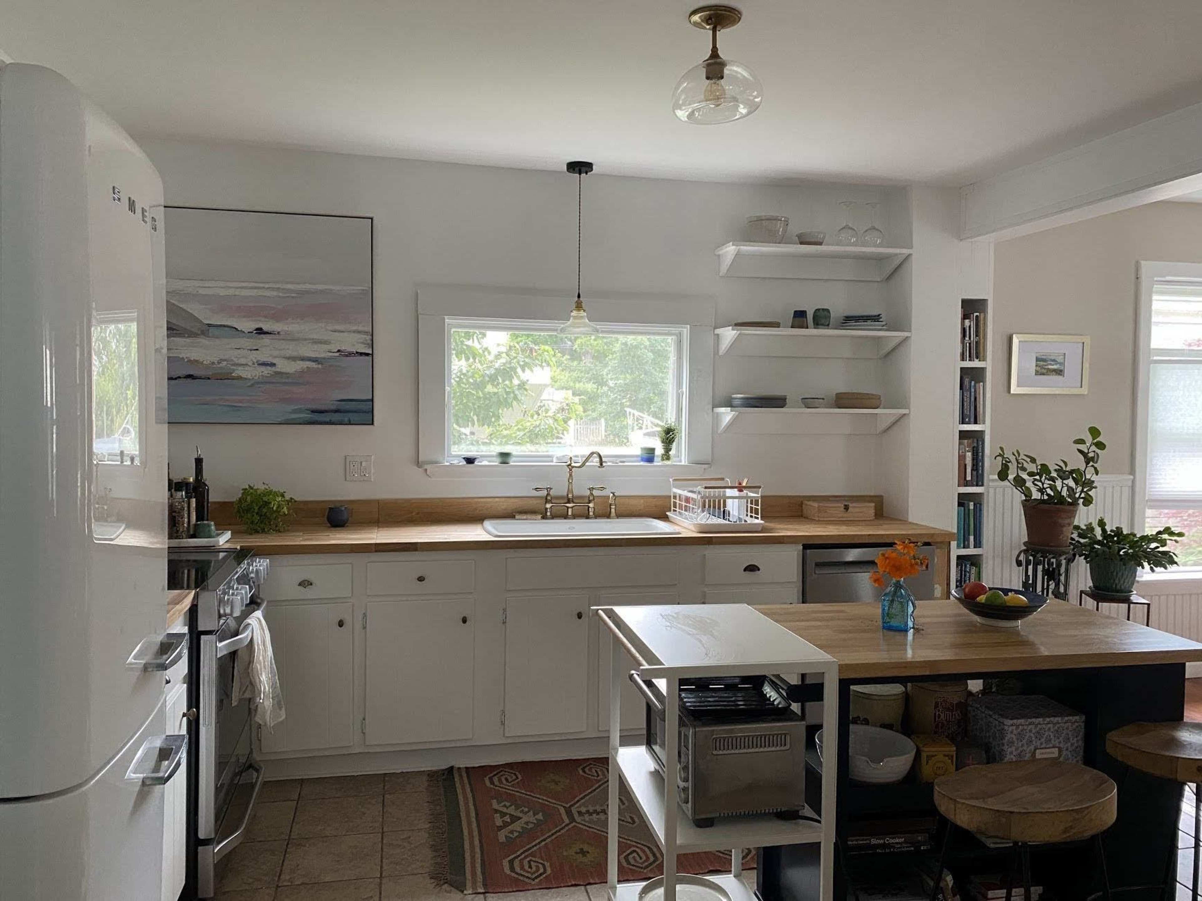A bright kitchen features white cabinets, a wooden countertop, and a view of greenery through a window.