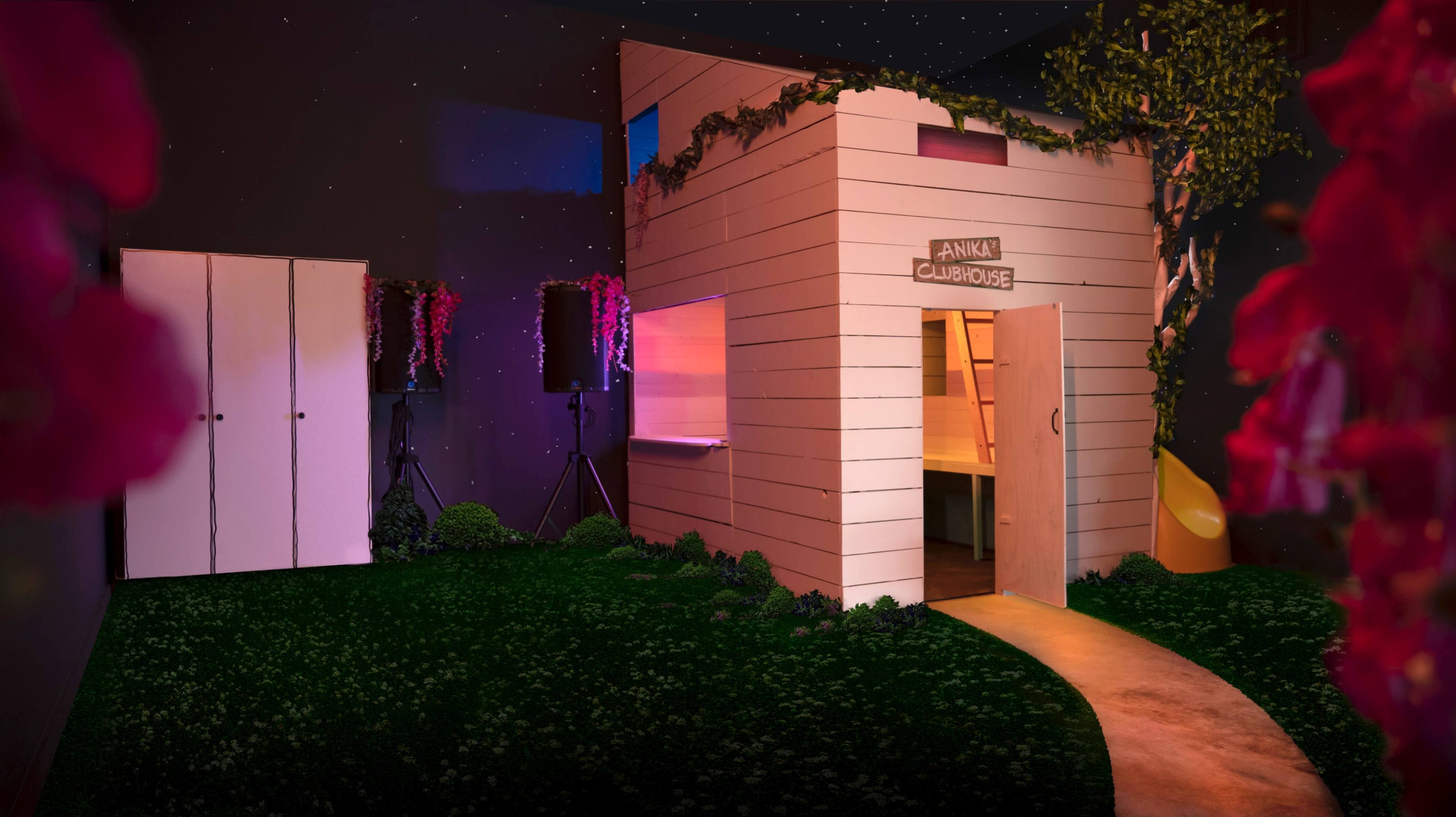 A small, modern white building surrounded by greenery and illuminated by soft lights, with a path leading to its entrance.