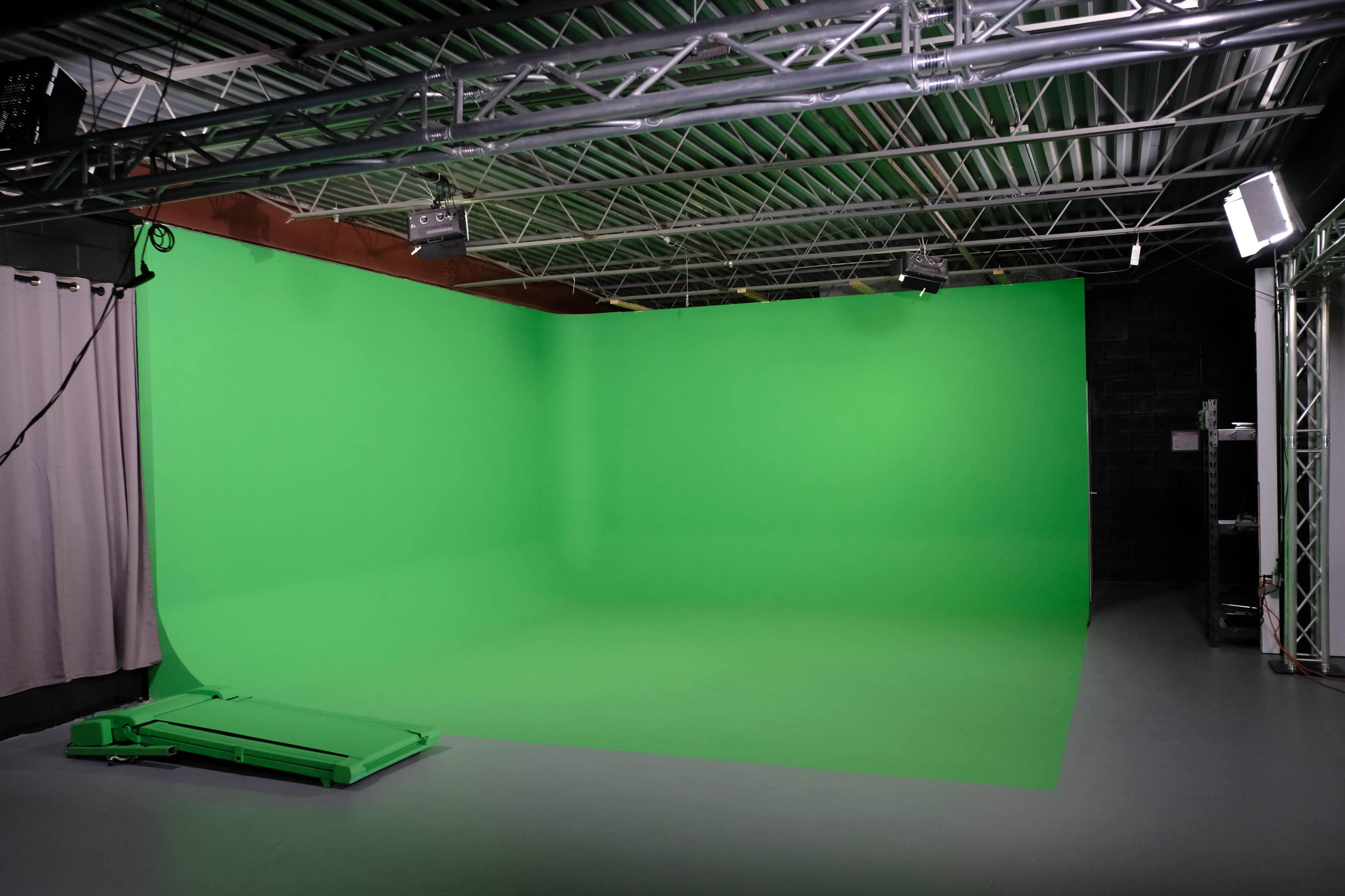 The image shows a spacious studio with a green screen backdrop and metal lighting fixtures overhead.