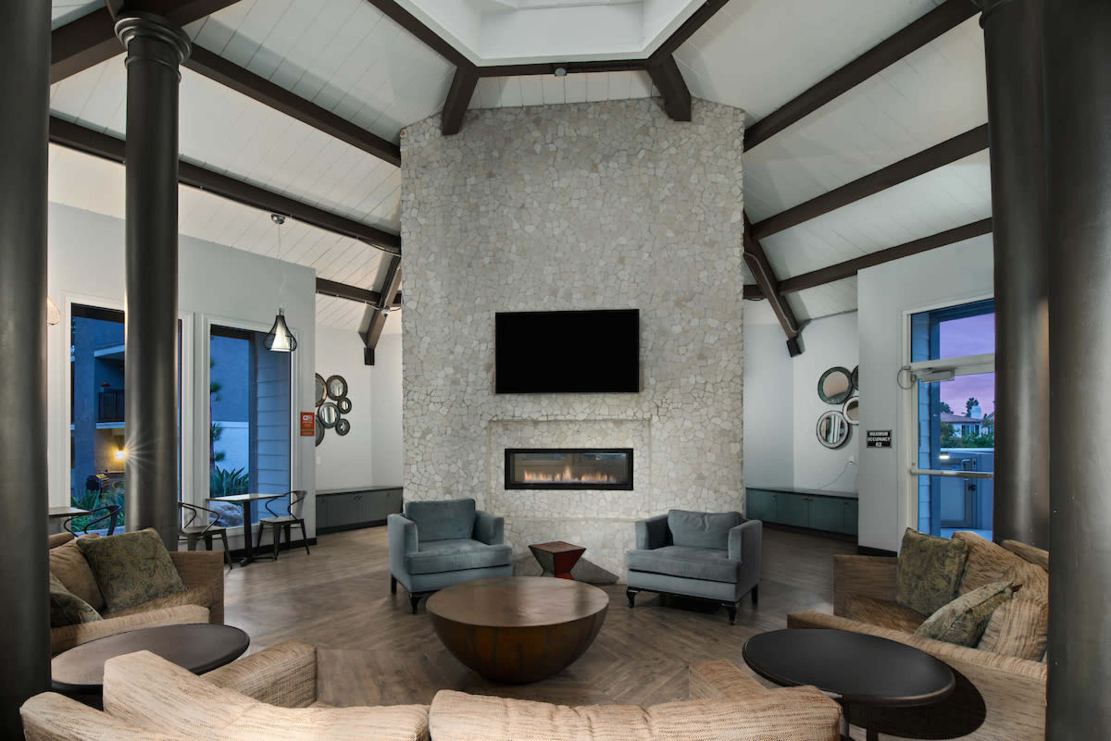 A modern living space with a stone fireplace as the focal point, surrounded by seating arrangements and large windows.