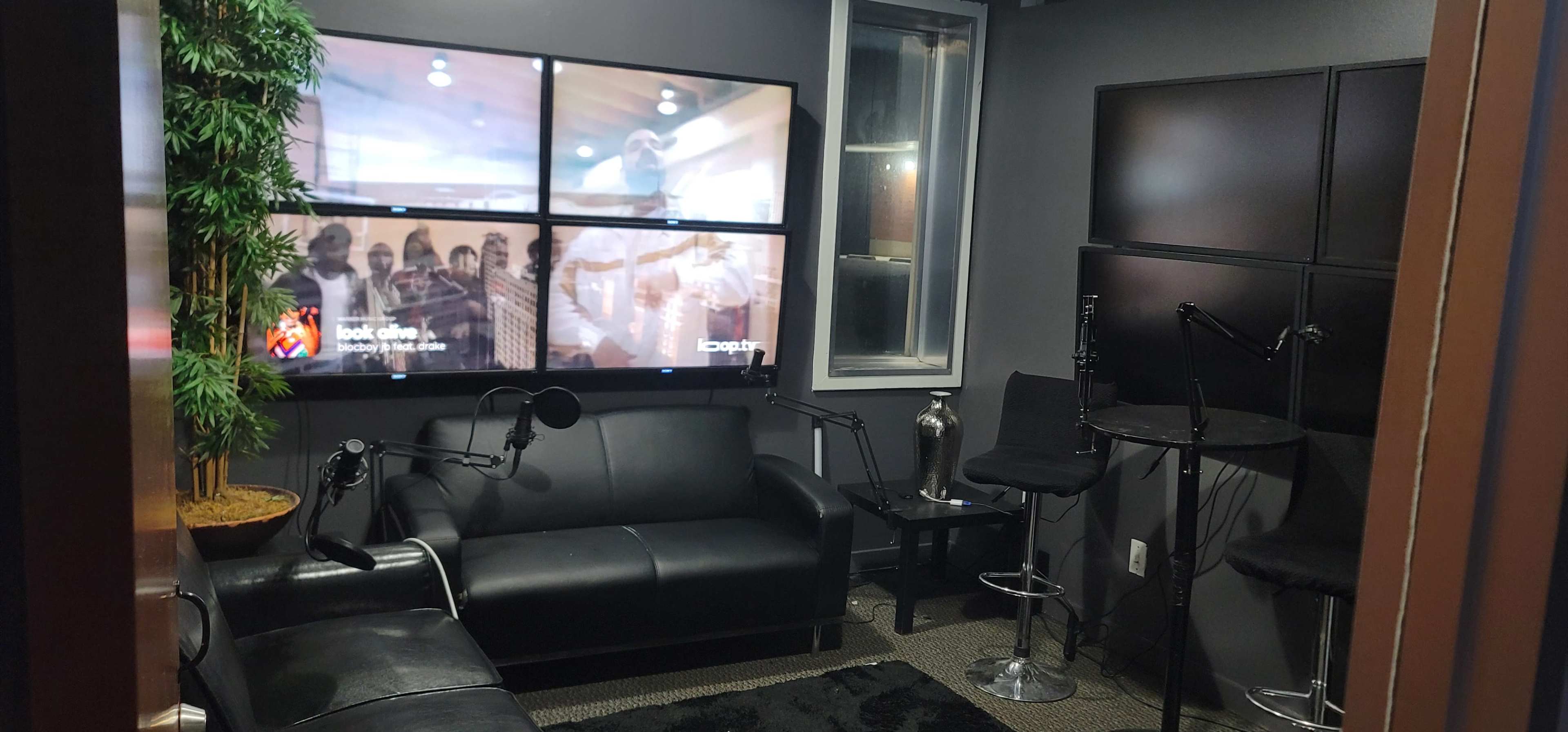 The room features a black leather couch, several high tables with stools, and a wall-mounted display made up of multiple screens.
