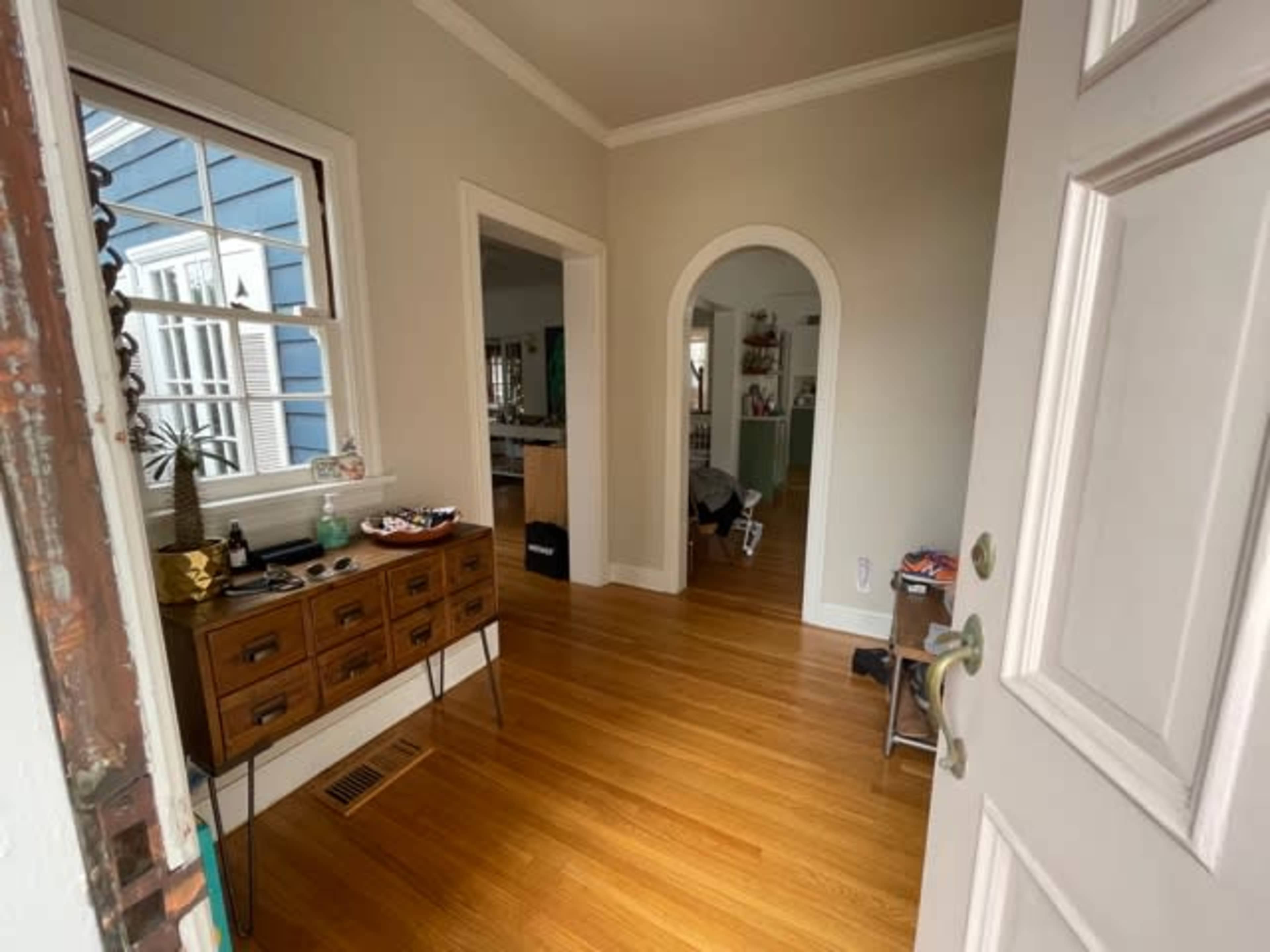 An entrance hallway with a wooden console table, arched doorway, and hardwood flooring.