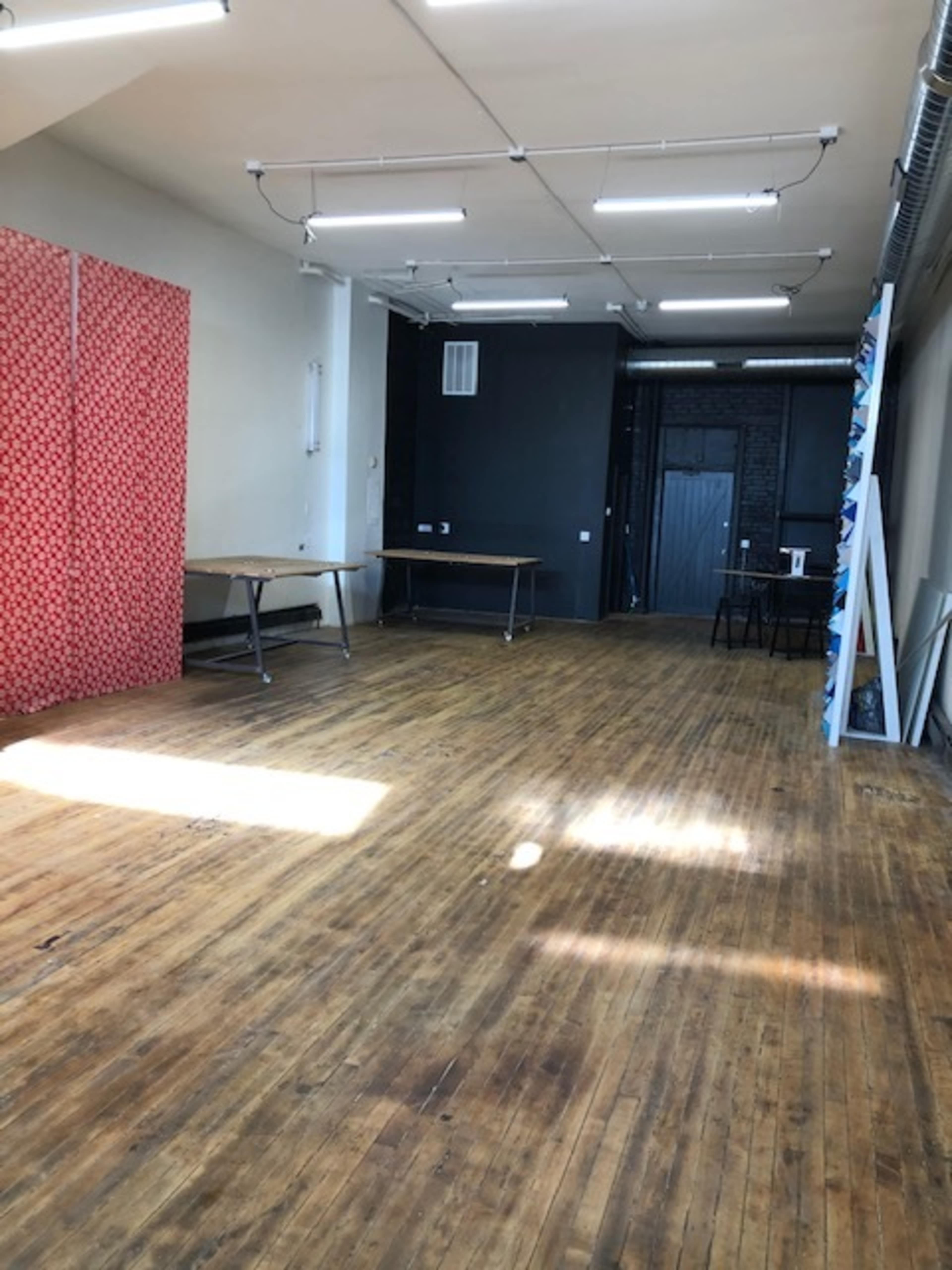 An empty room with wooden floors, a red patterned wall on one side, and several tables placed in the space.