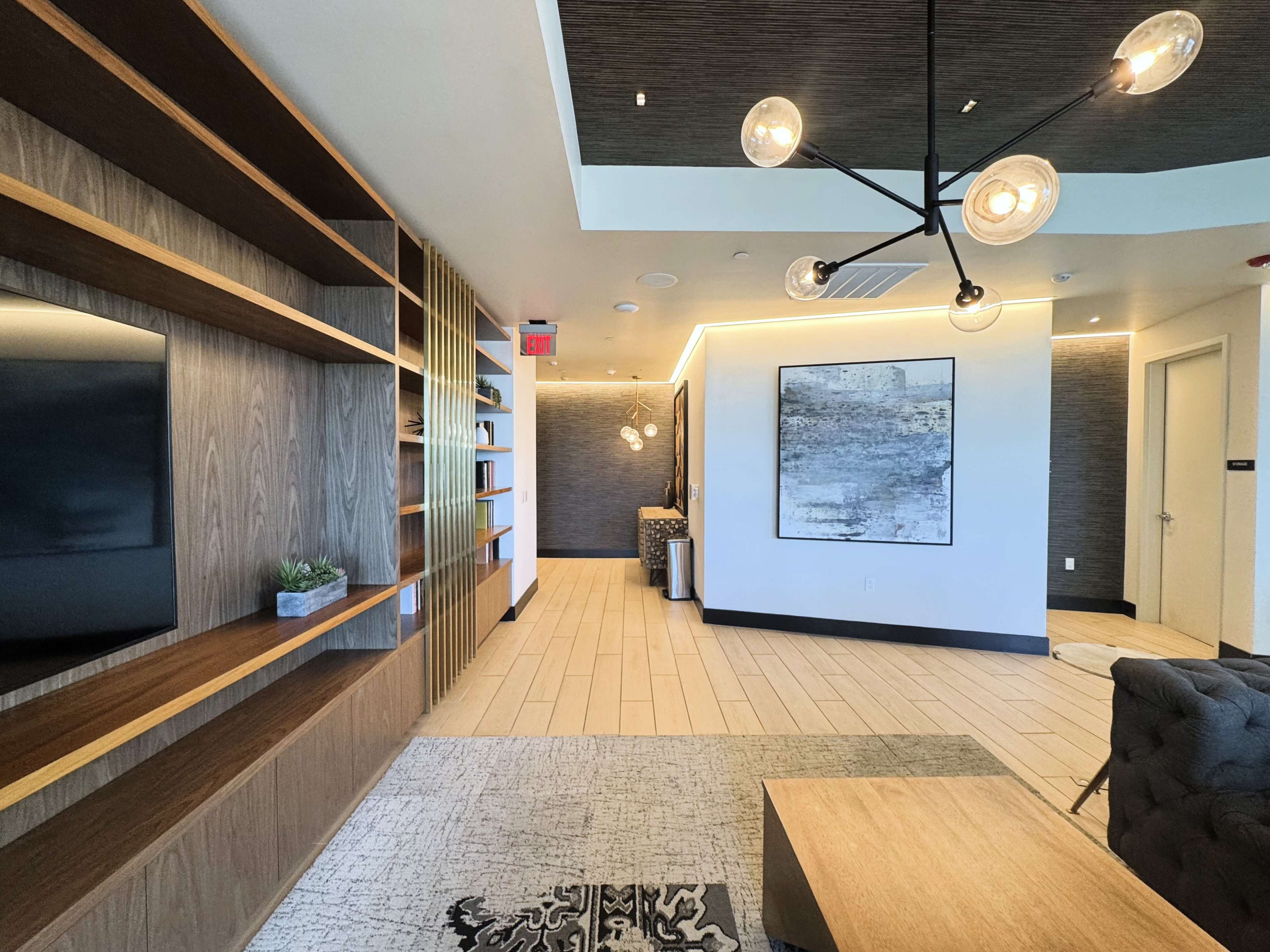 The image shows a modern interior space with a wooden shelf, a couch, a television, and artwork on the walls, illuminated by stylish light fixtures.