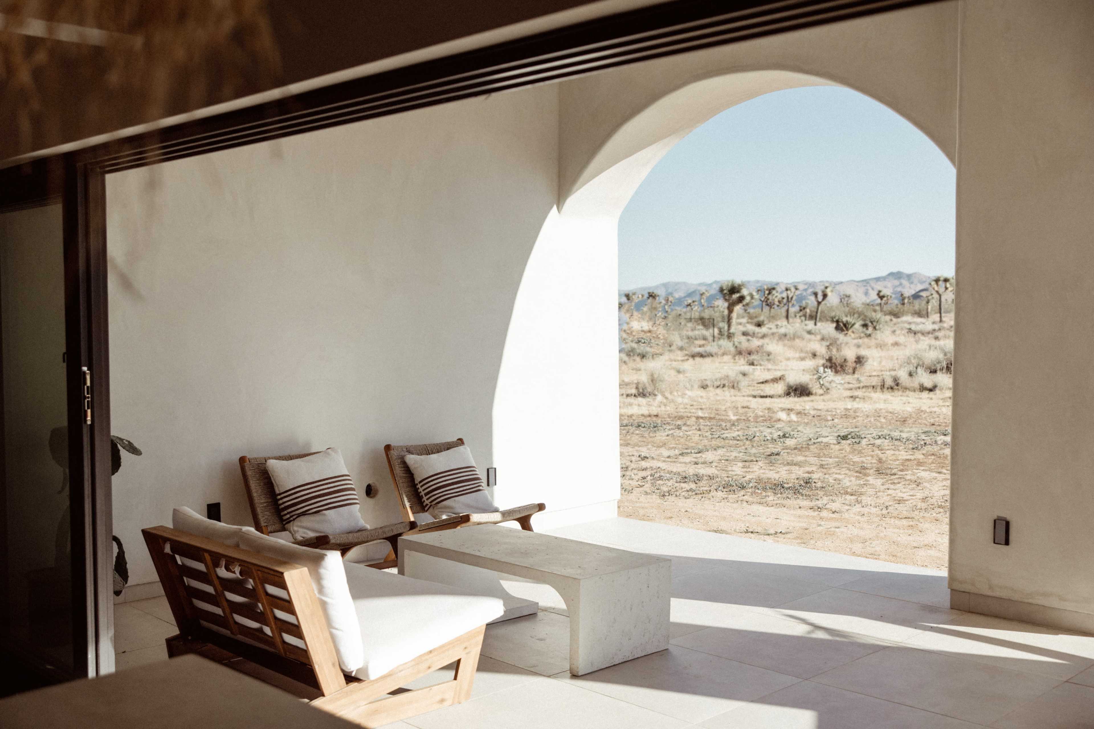 A minimalistic outdoor seating area with two chairs and a table, framed by an archway that opens to a desert landscape.