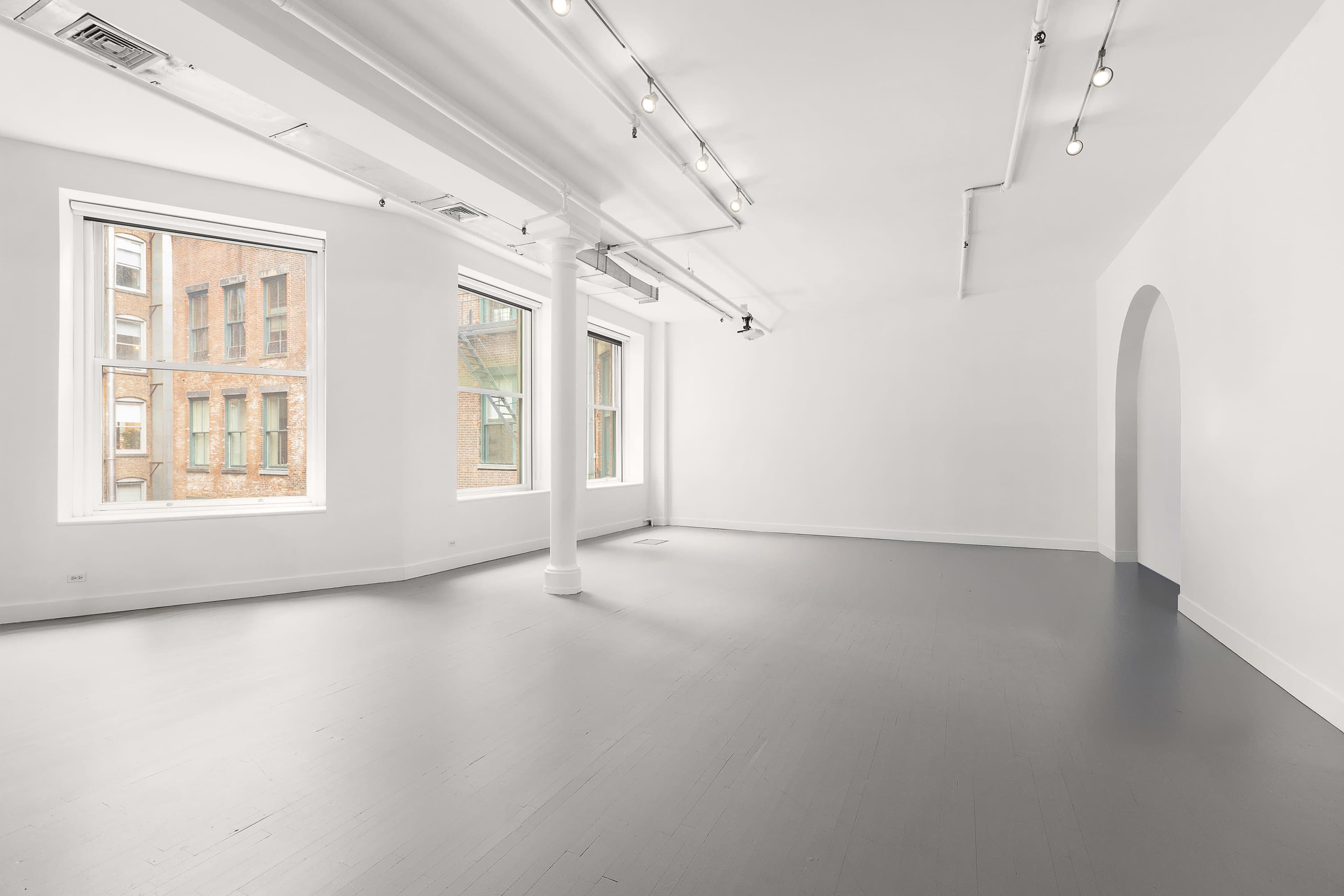 The image shows a spacious, empty room with gray flooring and large windows that let in natural light.