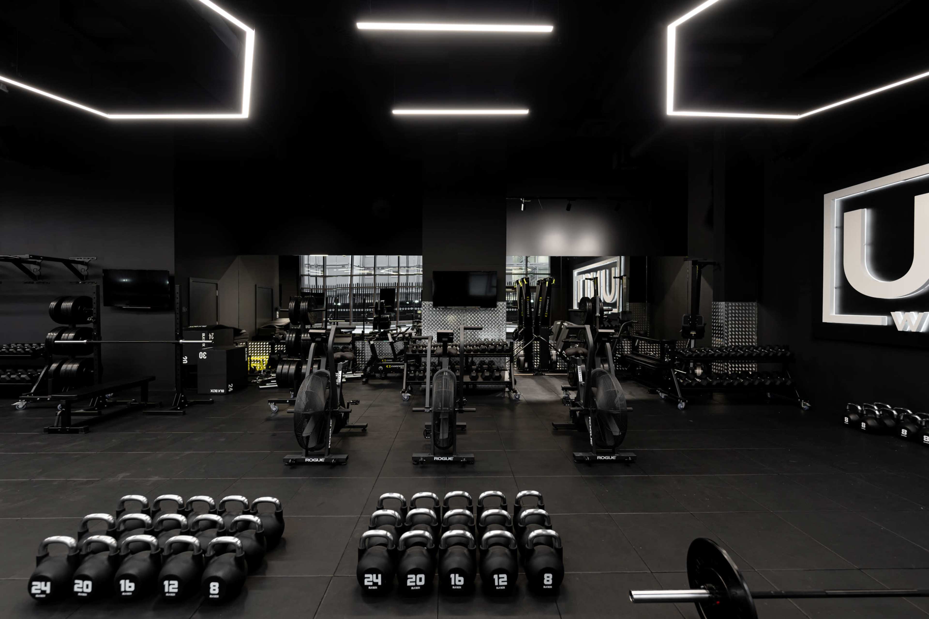 A modern gym interior equipped with various weightlifting equipment, including dumbbells and rowing machines, under bright ceiling lights.