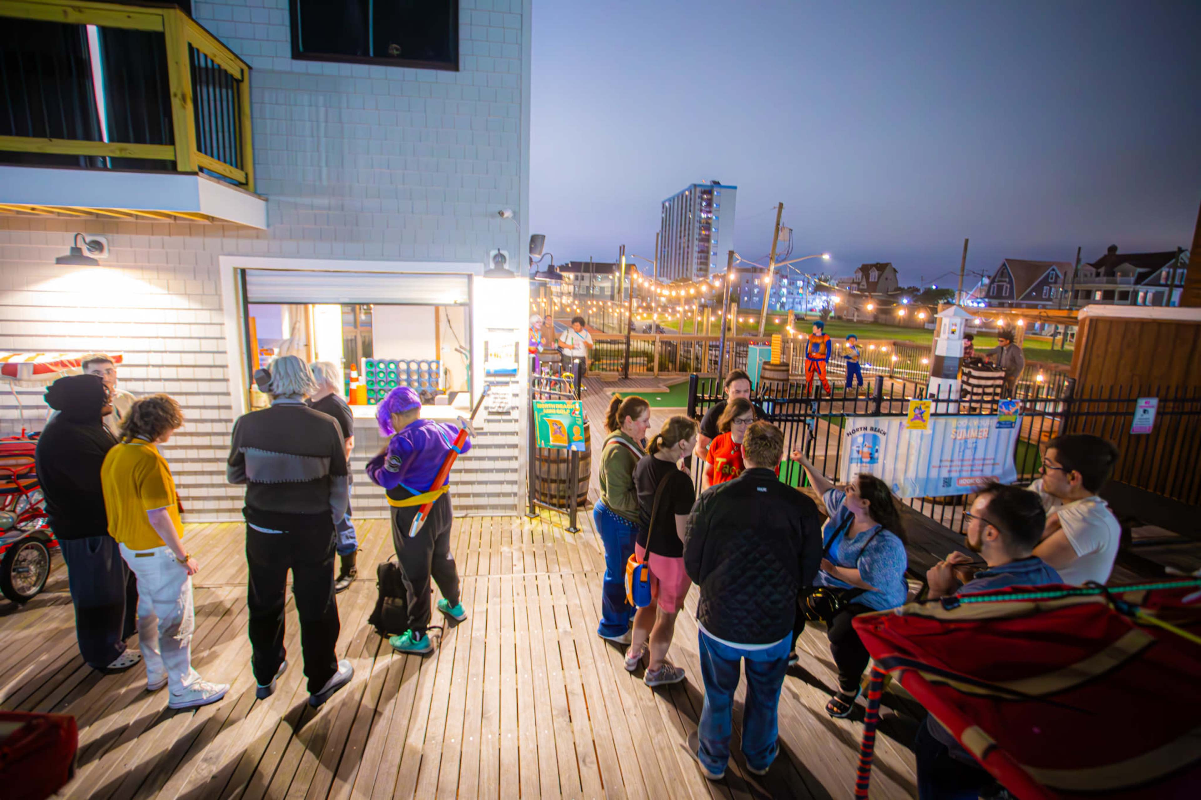A group of people gathers outside a building at night, with colorful lights and a playground visible in the background.
