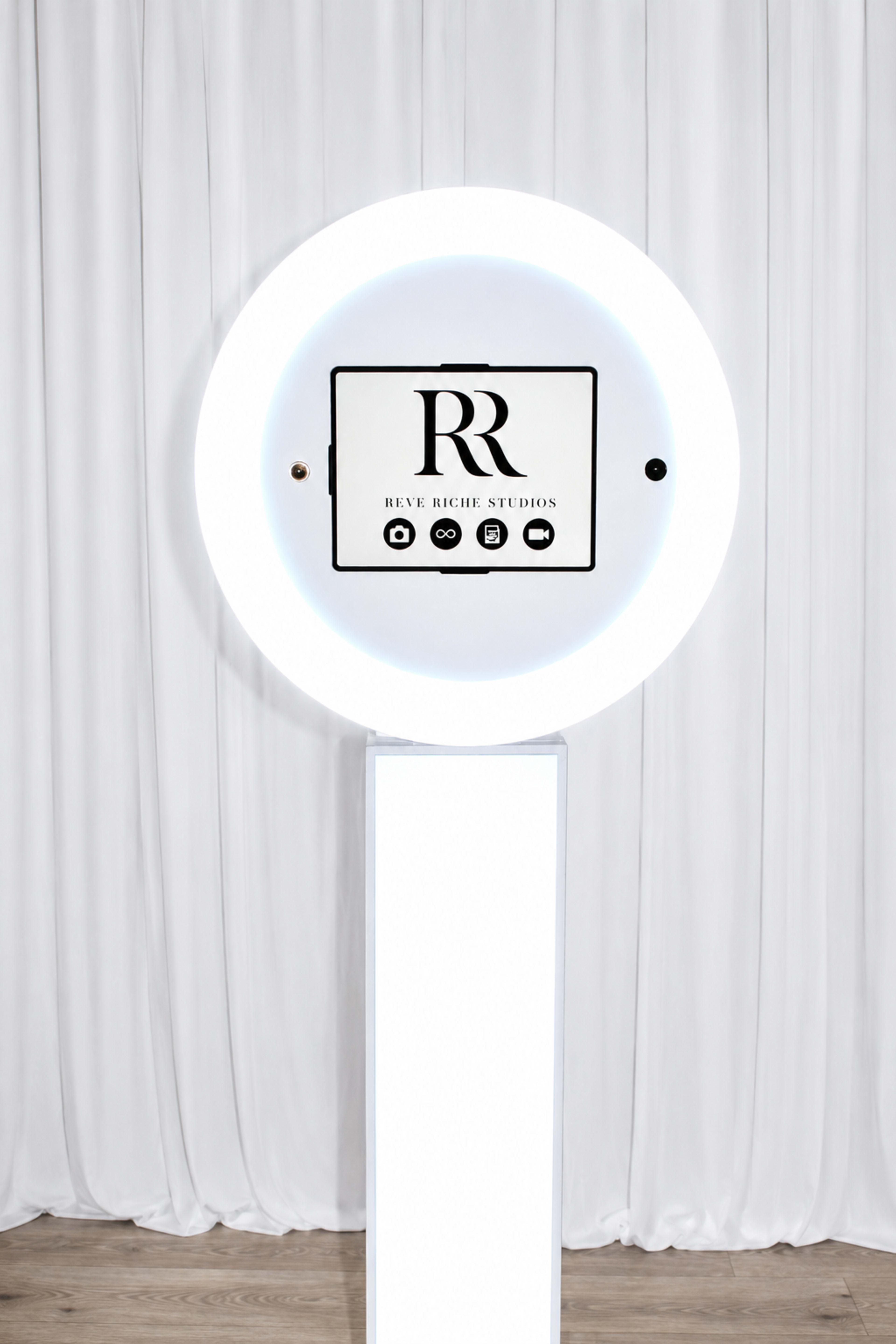 The image features a circular lighted display showcasing the logo for "Rêve Rich Studios" on a white pedestal in front of a draped backdrop.