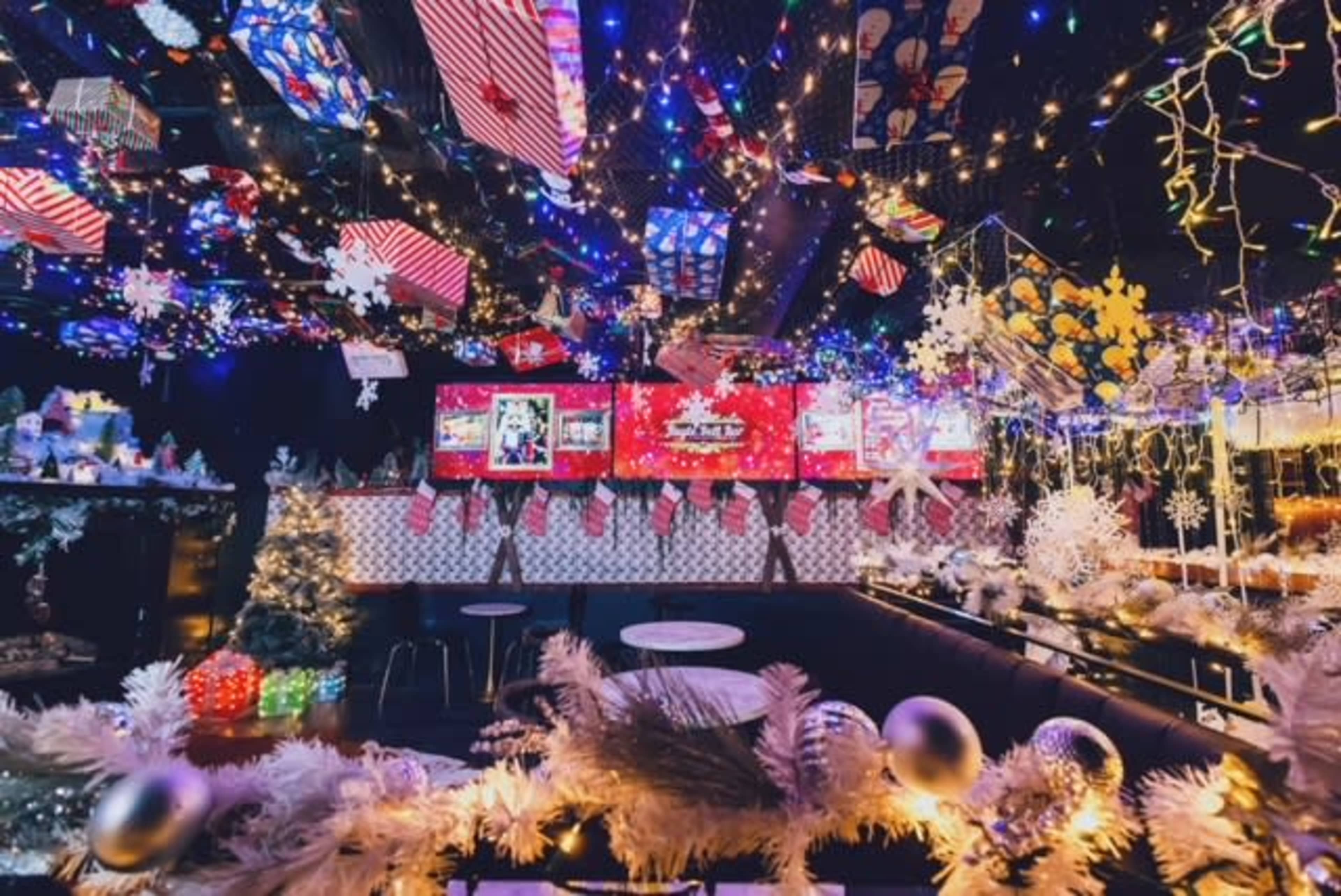 The image shows a festive indoor space decorated with colorful lights, holiday decorations, and various ornaments, creating a cheerful atmosphere.