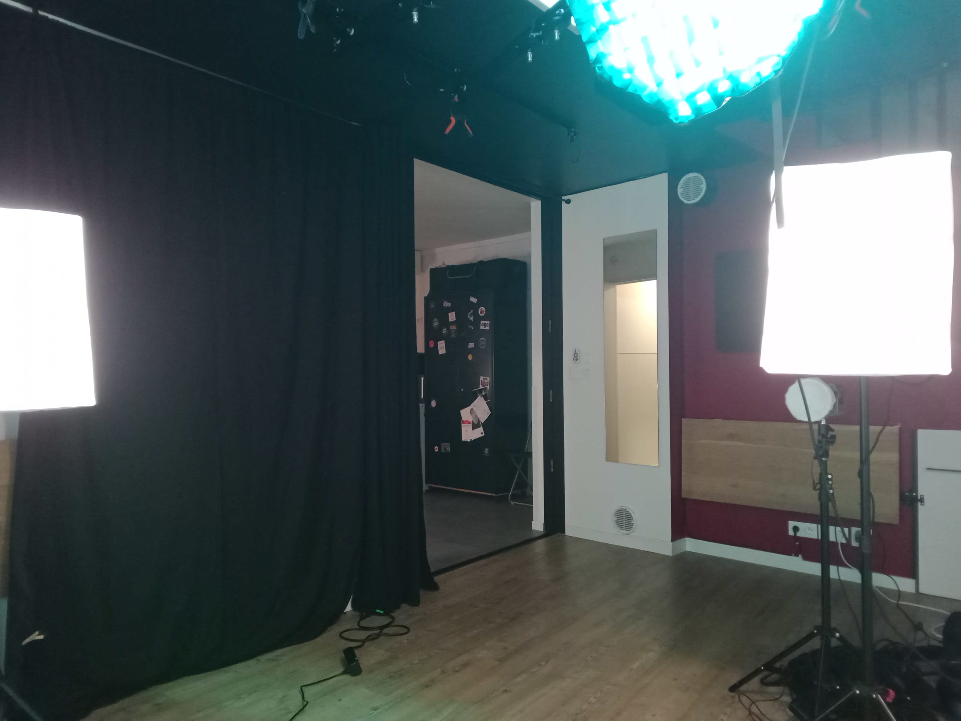 The image shows a dimly lit studio space with black curtains, two softbox lights, and a doorway leading to another room.
