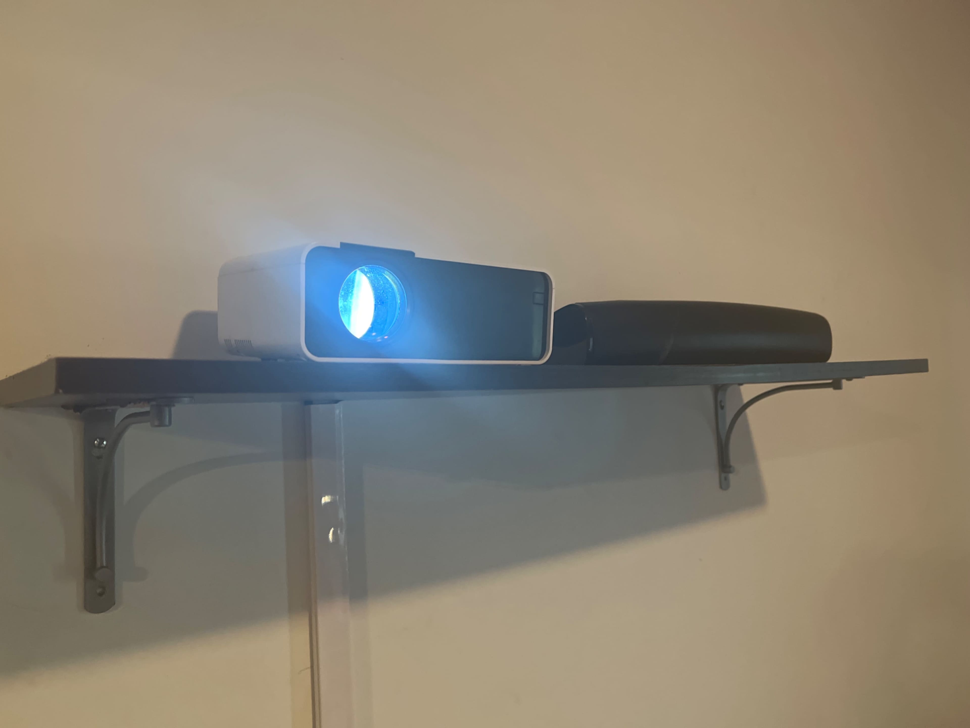 A projector positioned on a shelf projects a blue light against a wall.