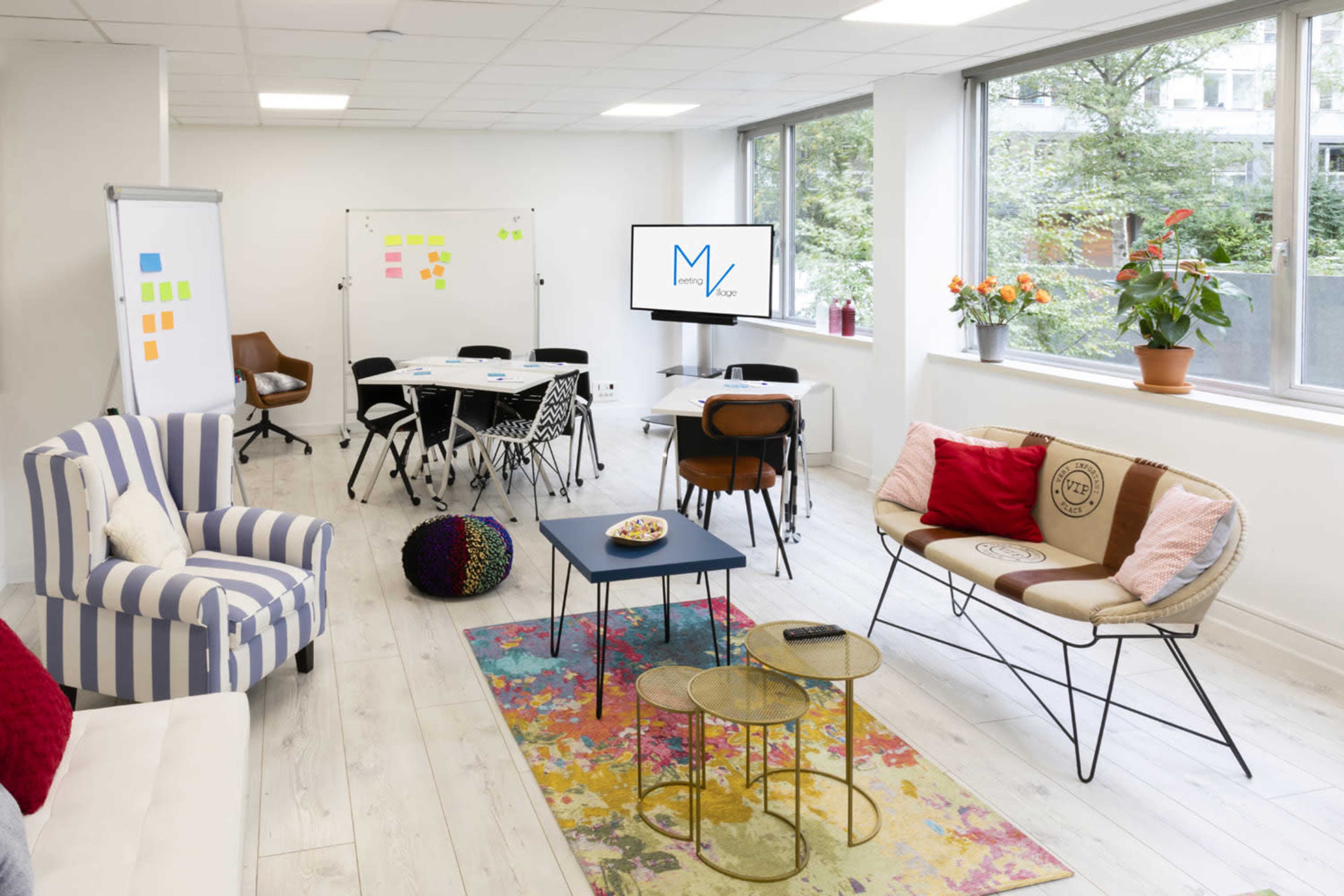 A modern office space with a seating area, a conference table, whiteboards, and large windows letting in natural light.