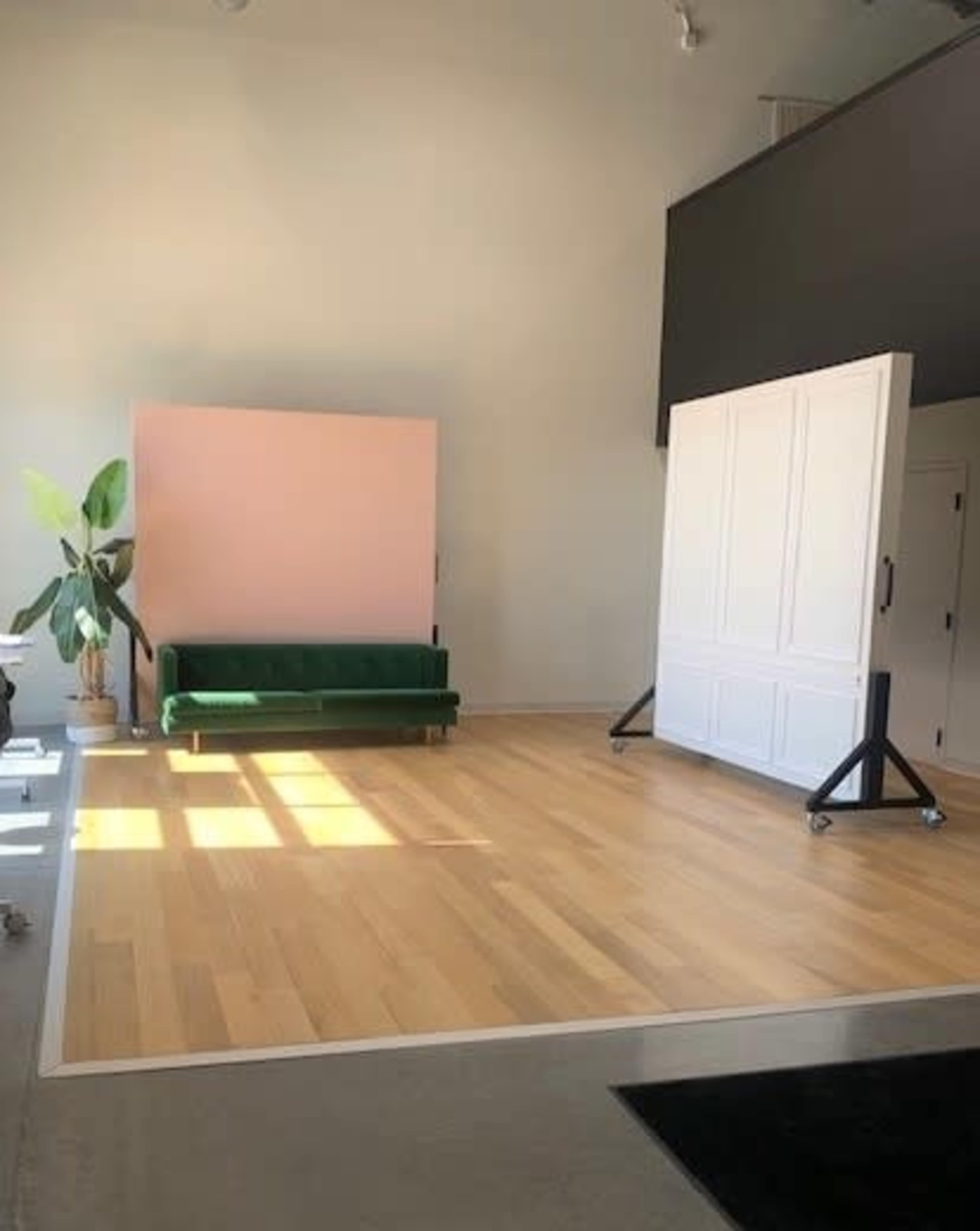 A spacious room with a green sofa, a pink backdrop, and a large white panel set on wheels, all arranged on a wooden floor.